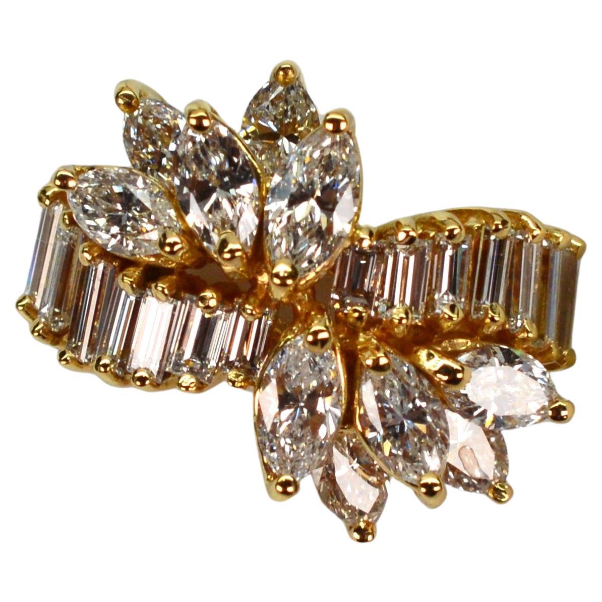 A double band of 18 karat yellow gold hosts a luminous ribbon of fourteen emerald cut diamonds that sweep across the ring's facade in an asymmetrical design. A high profile cluster of twelve marquis diamonds add an impressive finishing detail on