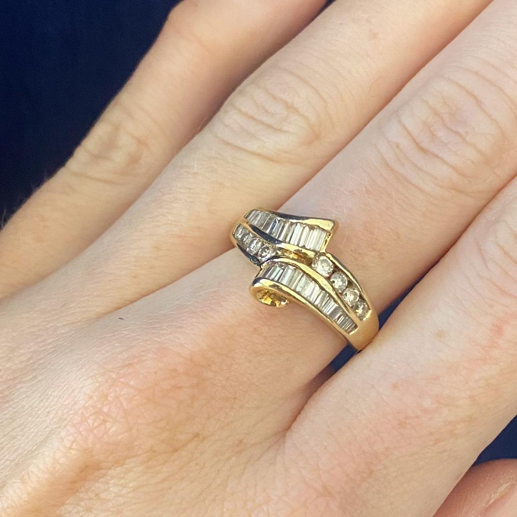 This fabulous ribbon ring is like winning a prize that you can wear on your hand, like a curling sash of sparkle on the finger! Baguette diamonds curve past each other at the center with a line of round brilliant diamonds for an accent of sparkles.