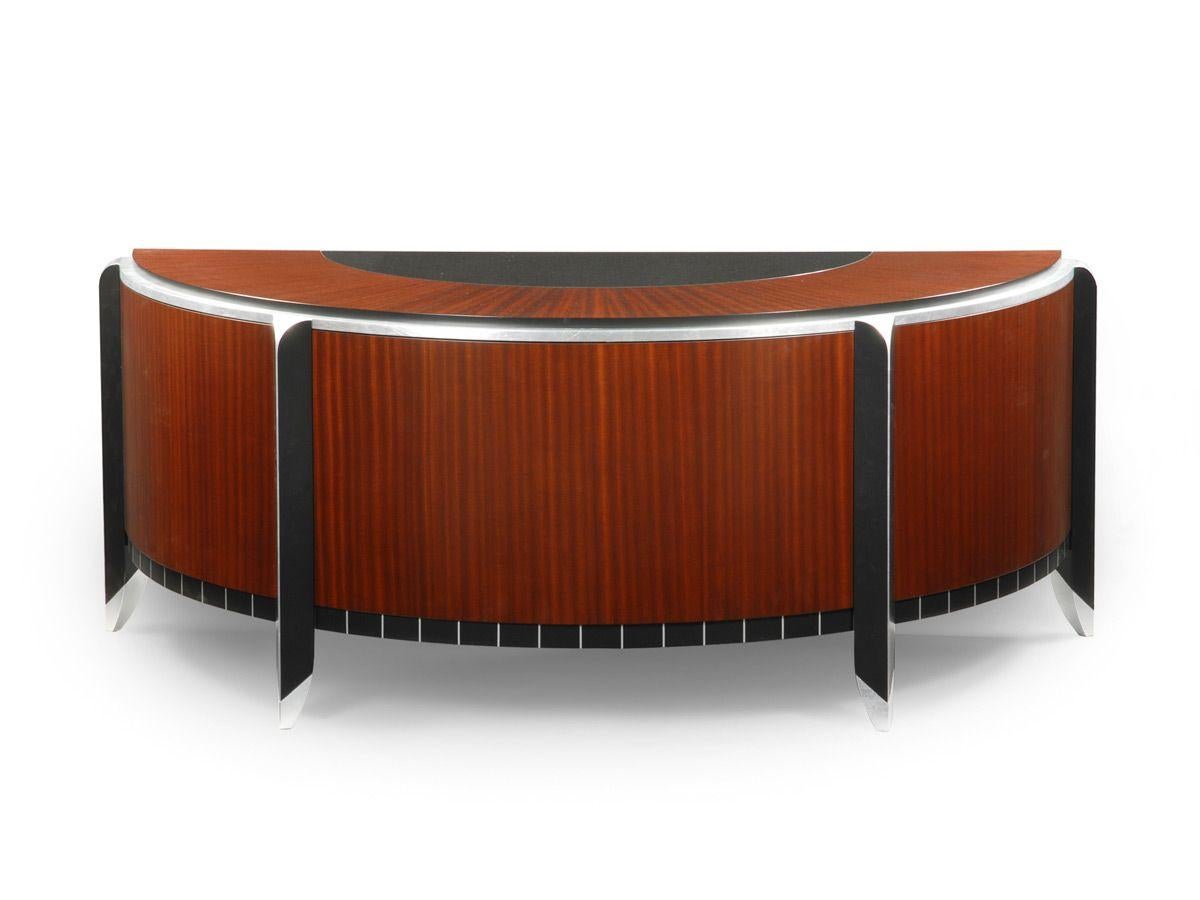 This exquisite executive desk features a semi-circular black granite inset top with a sunburst ribbon Sapele top border. Ribbon Sapele façade with black and metal leaf detailing. One center pencil drawer, two box drawers on one side, adjustable