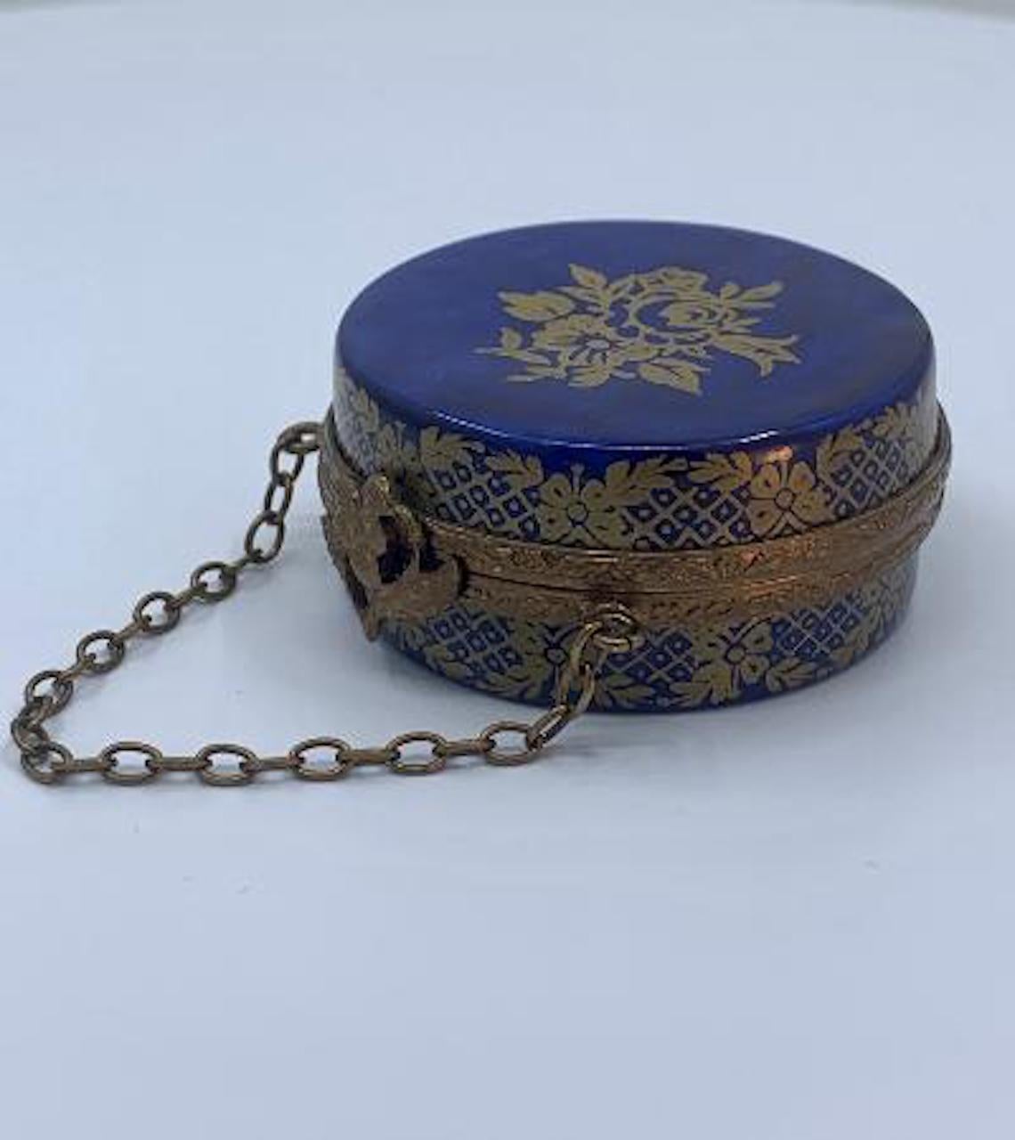 Very pretty, Limoges porcelain miniature hat box or round purse shaped trinket box is handmade and hand painted in France and features a beautiful cobalt blue field with rich 24 Karat gold floral motif accents. Box features antiqued gold gilt metal