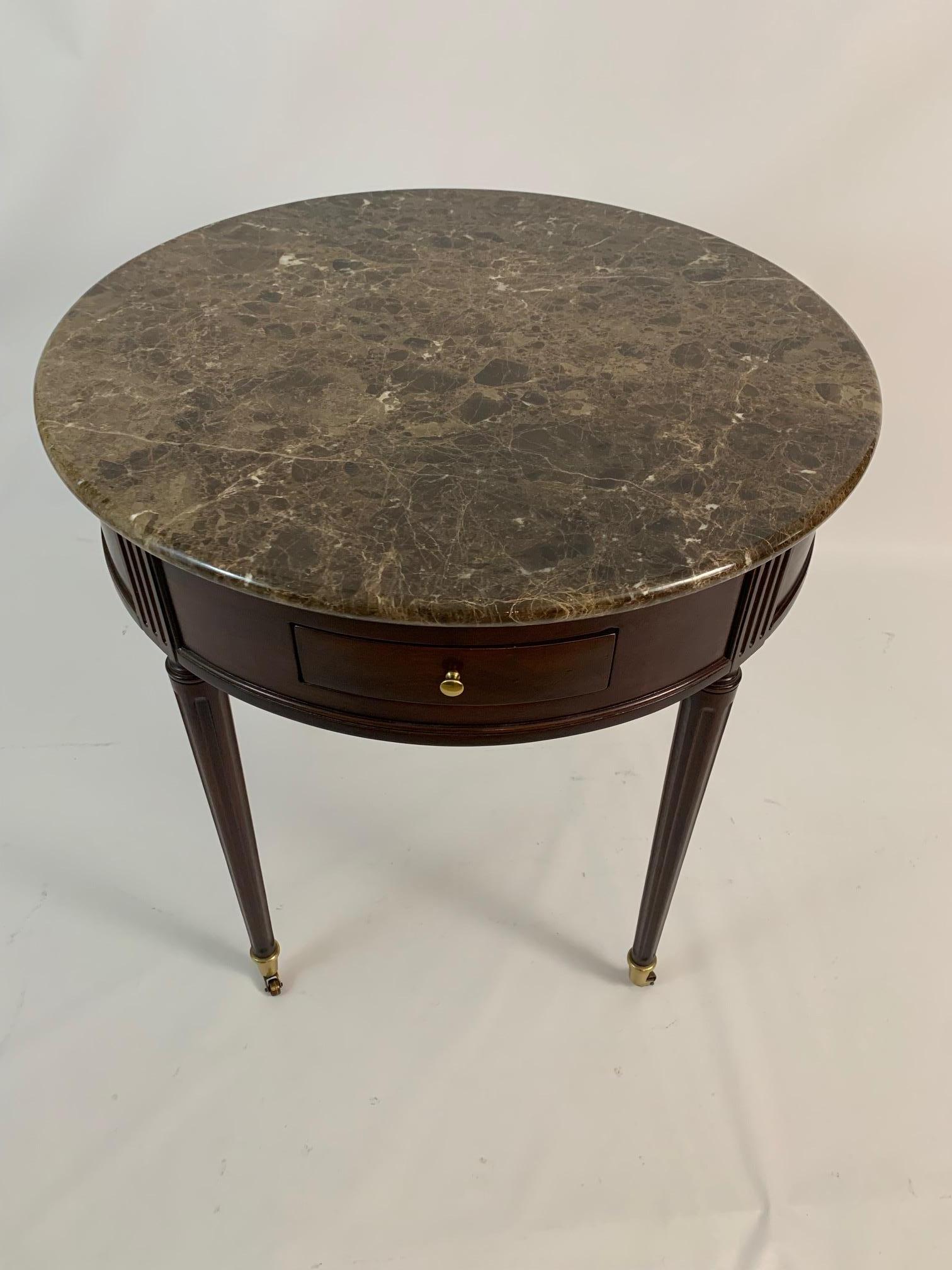 A rich & elegant round mahogany side table having 2 drawers and 2 pull out leather slides as well as a sumptuous marble top. Legs are tapered and terminate in brass caps and casters. Biltmore Estate by Heritage Collection label.
 