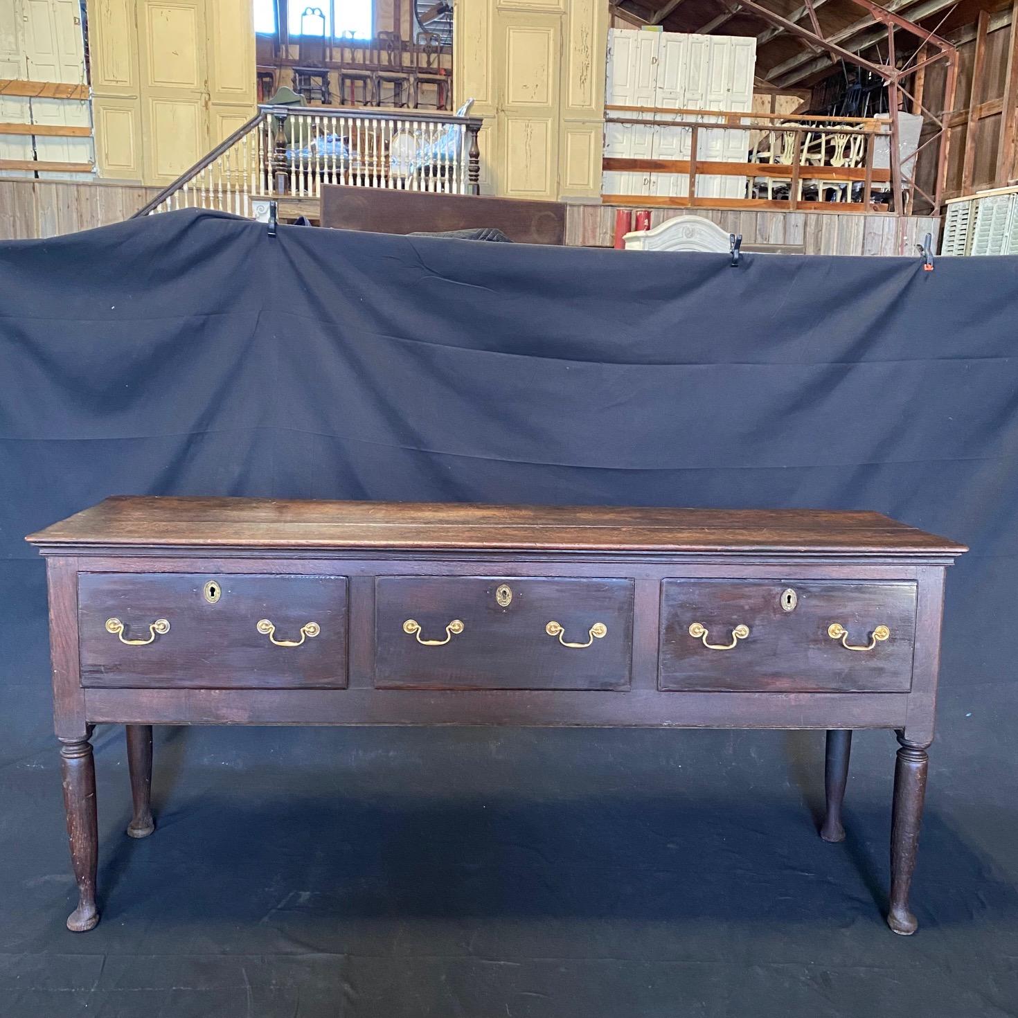 Oozing with antique character, an 18th Century Oak Welsh oak sideboard or buffet comprised of a rectangular top over three generous drawers, raised on lovely carved tapering legs. Later brass pulls with the correct period design. Bought in the South