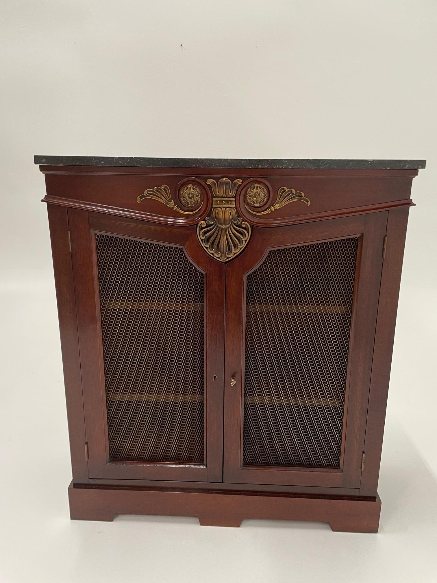 Richly crafted mahogany Regency style bookcase having raised fancy cartouche at the top, brass mesh doors and marble top. There are two adjustable shelves inside and key included.