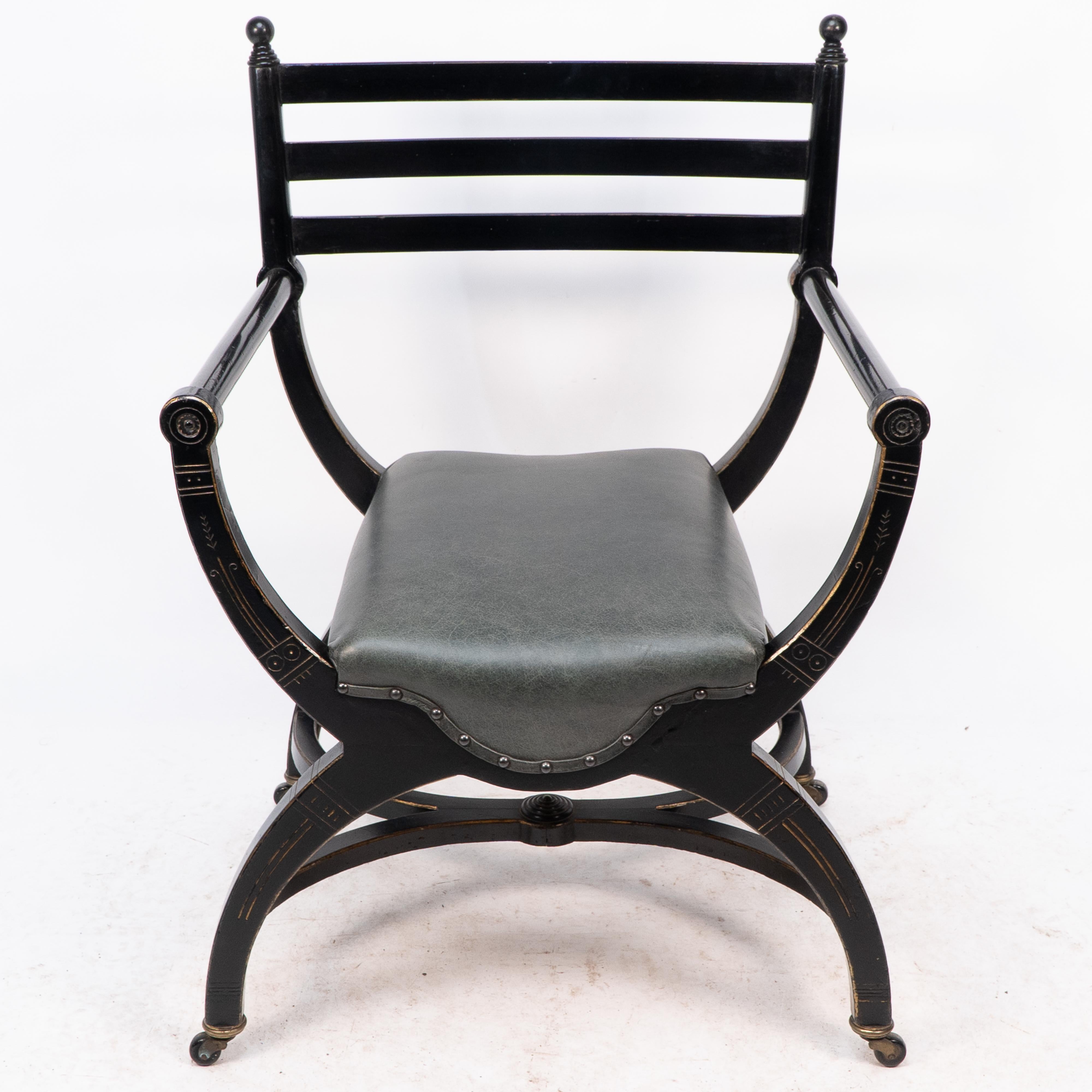 Richard Charles (1823-93), an Aesthetic Movement ebonized elbow chair, circa 1866, with ball finials, a ladder back, later leather seat, gilt highlights and X-frame base with X-frame stretcher, on casters, 83cm high. The attribution is based on the