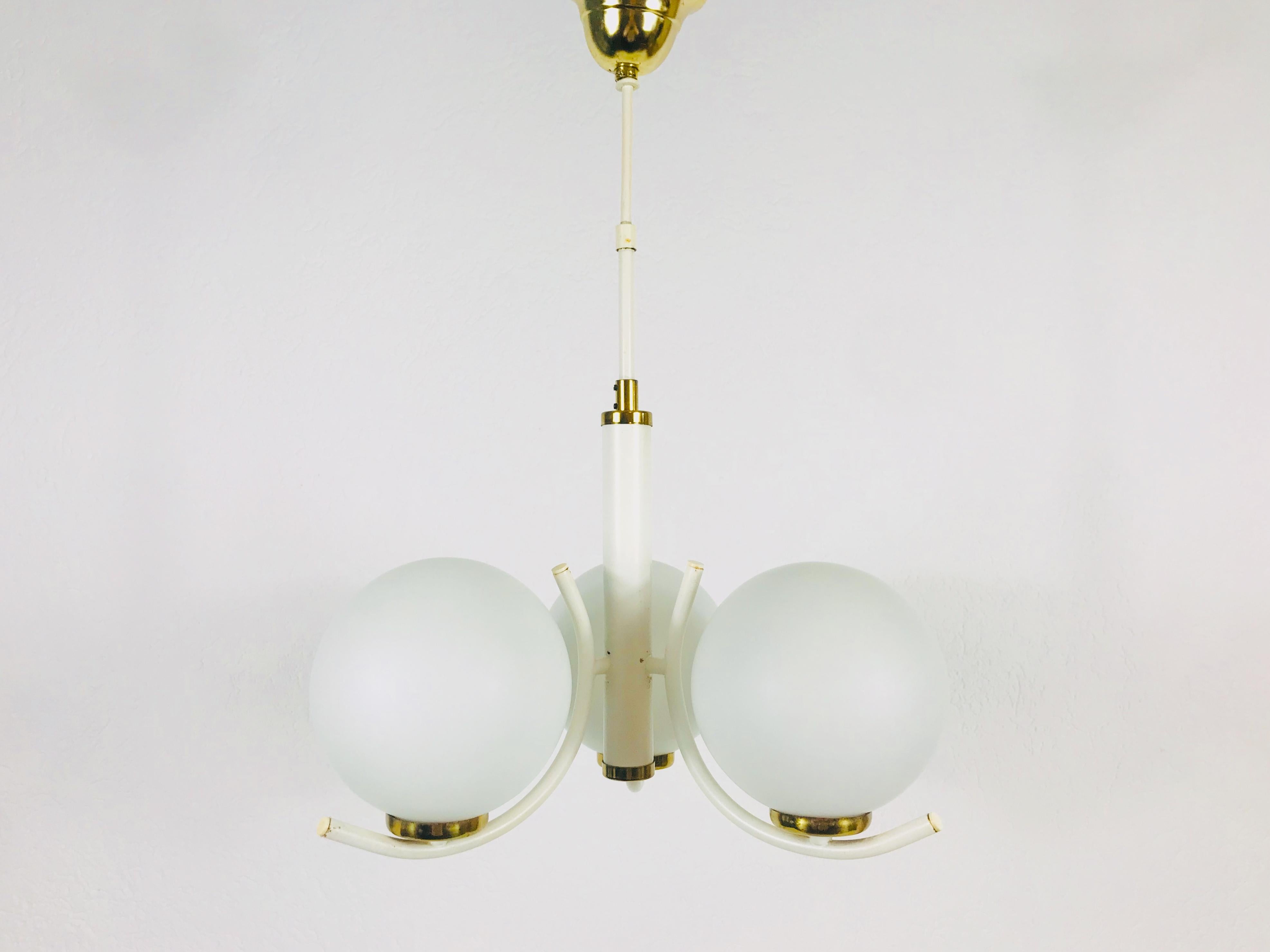 A Richard Essig chandelier made in Germany in the 1970s. It is fascinating with its elegant design. Three opaque glass balls which screw onto the metal body. There are brass parts as the bottom of the balls and also the bar is made of
