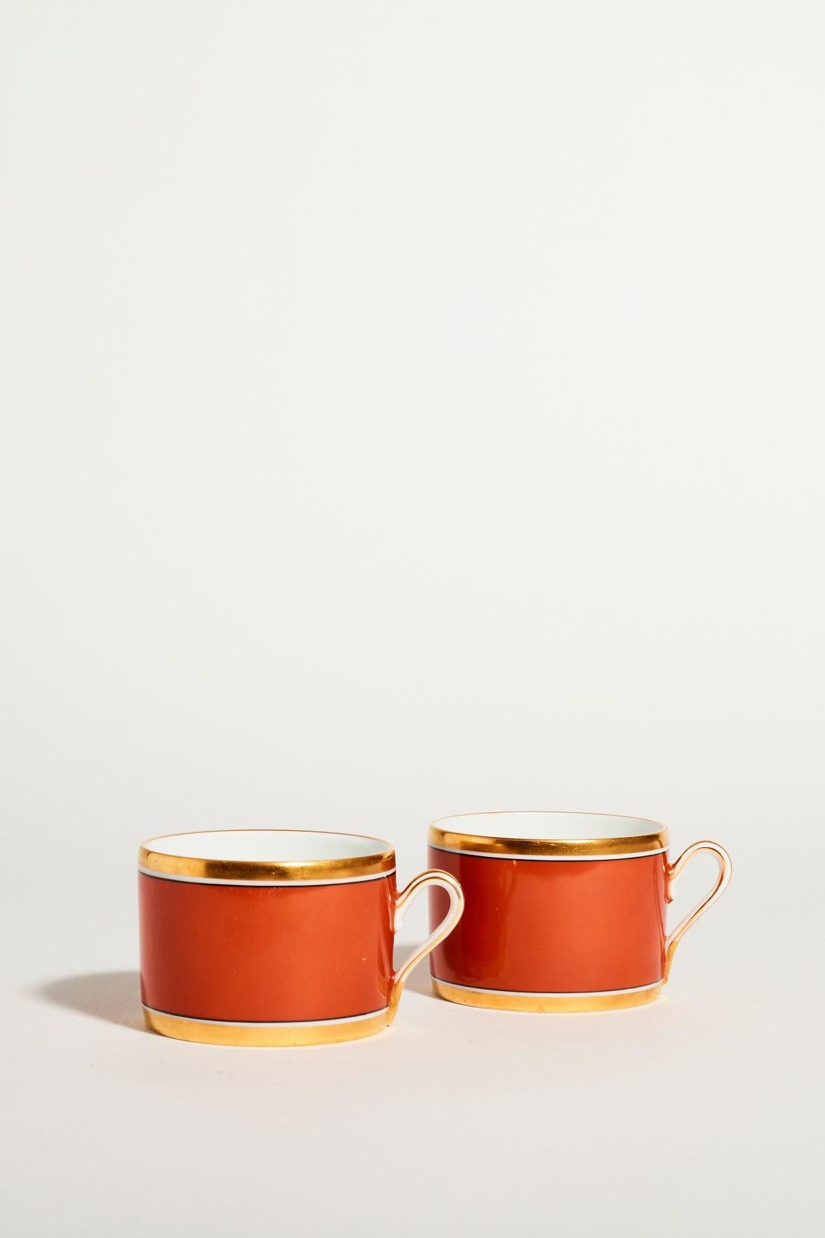 Richard Ginori quality porcelain coffee set of two, burnt orange contrasted against crisp white embellished with gold trim.