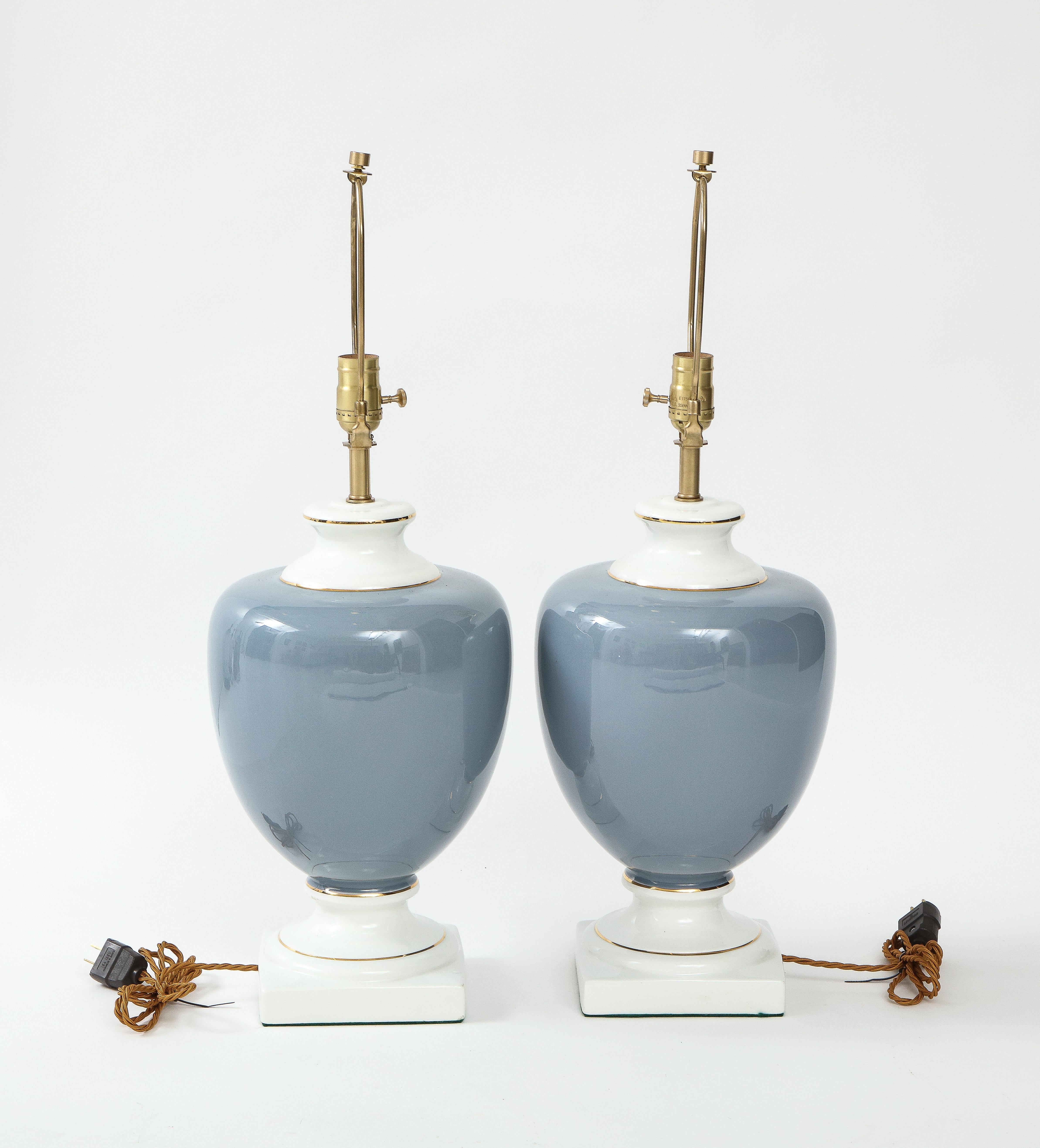 Pair of Neoclassical Urn shaped porcelain lamps featuring a french blue color and 22kt gold pinstripe detail. Lamps have been rewired to USA standards, 100W max bulbs. Square base measures 6