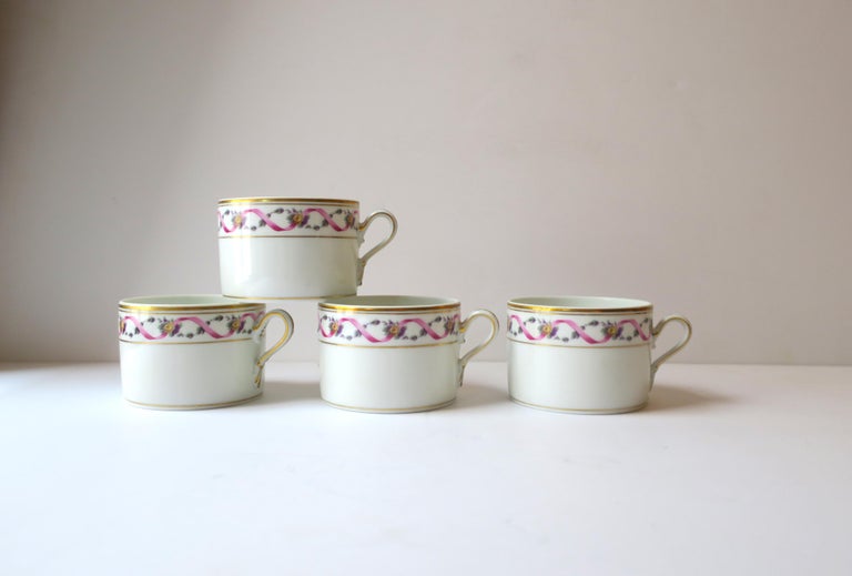 A beautiful set of four (4) Richard Ginori Italian porcelain coffee or teacups, circa late-20th century, 1980s, Italy. Cups are white glazed porcelain with gold detail on lip, rim, base, and handle, and a pink ribbon and purple and green floral
