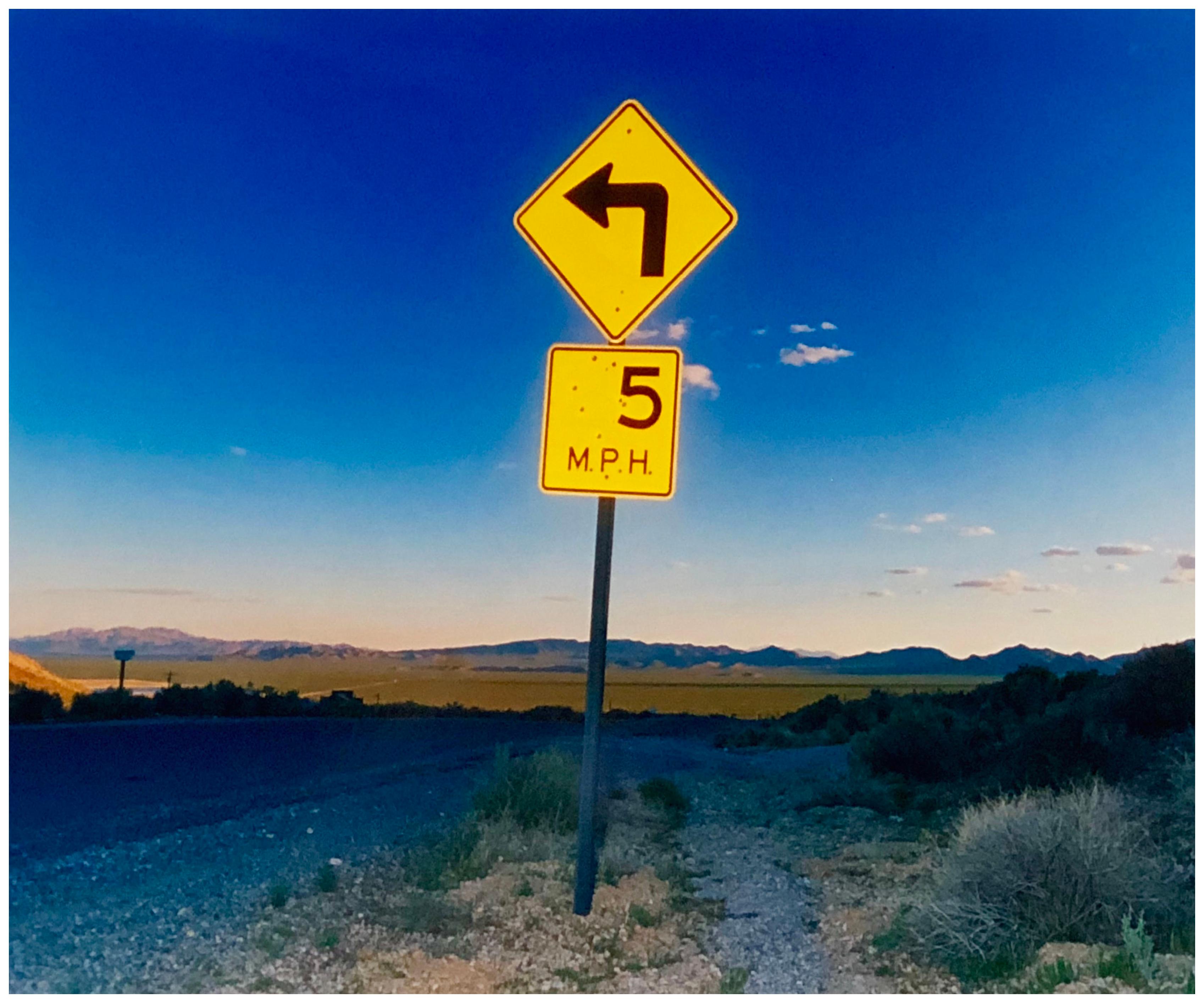 Five Miles Per Hour, Rhyolite, Nevada, photograph from Richard Heeps 'Dream in Color' Series. This photograph taken at dusk captures the sunset in the valley.  The area was once a goldmine, now a ghost town. The sign, 5MPH is so cautious but on