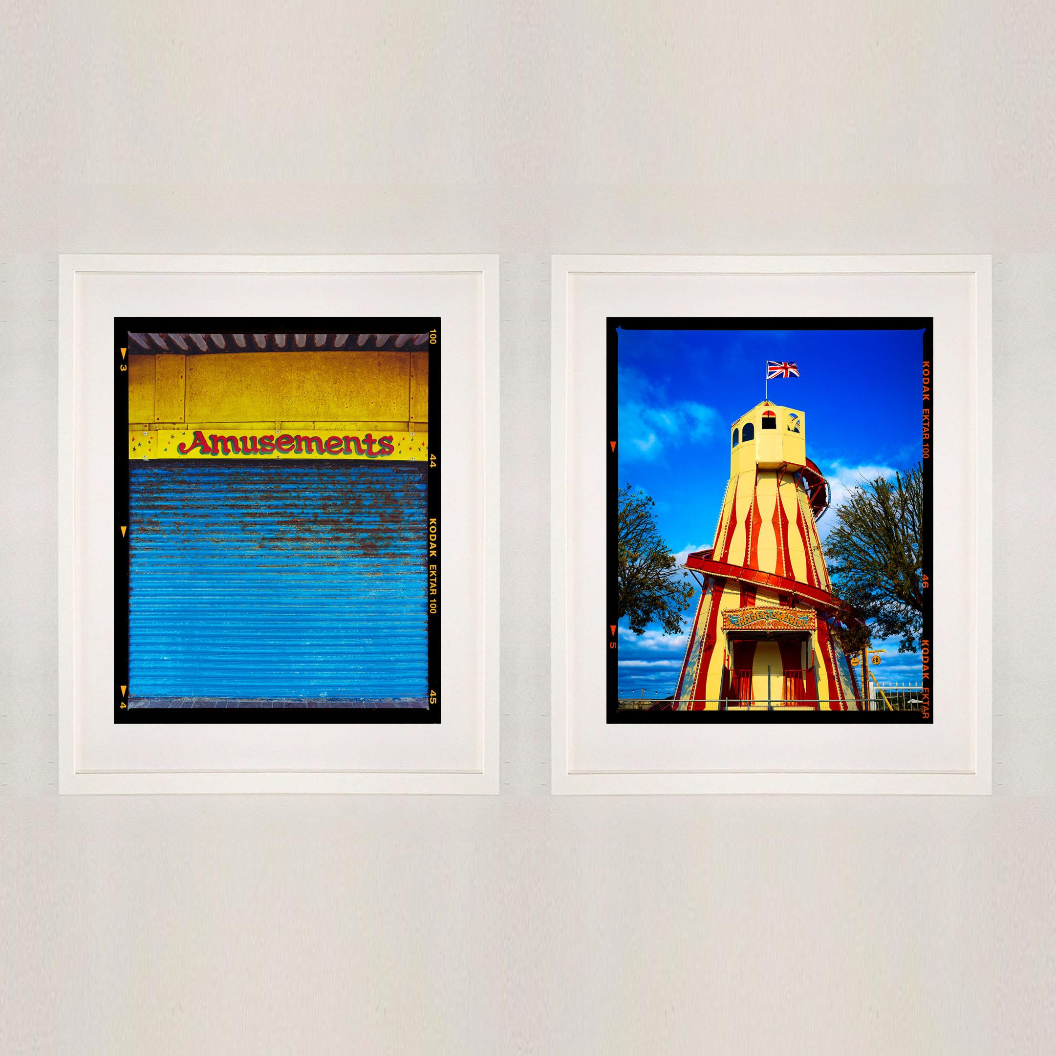 Helter Skelter, fotografia vintage britannica di un luna park della serie Norfolk, On-Sea di Richard Heeps. L'opera d'arte cattura un vivace elicottero a strisce gialle e rosse contro un cielo blu brillante, mentre la bandiera dell'Union Jack