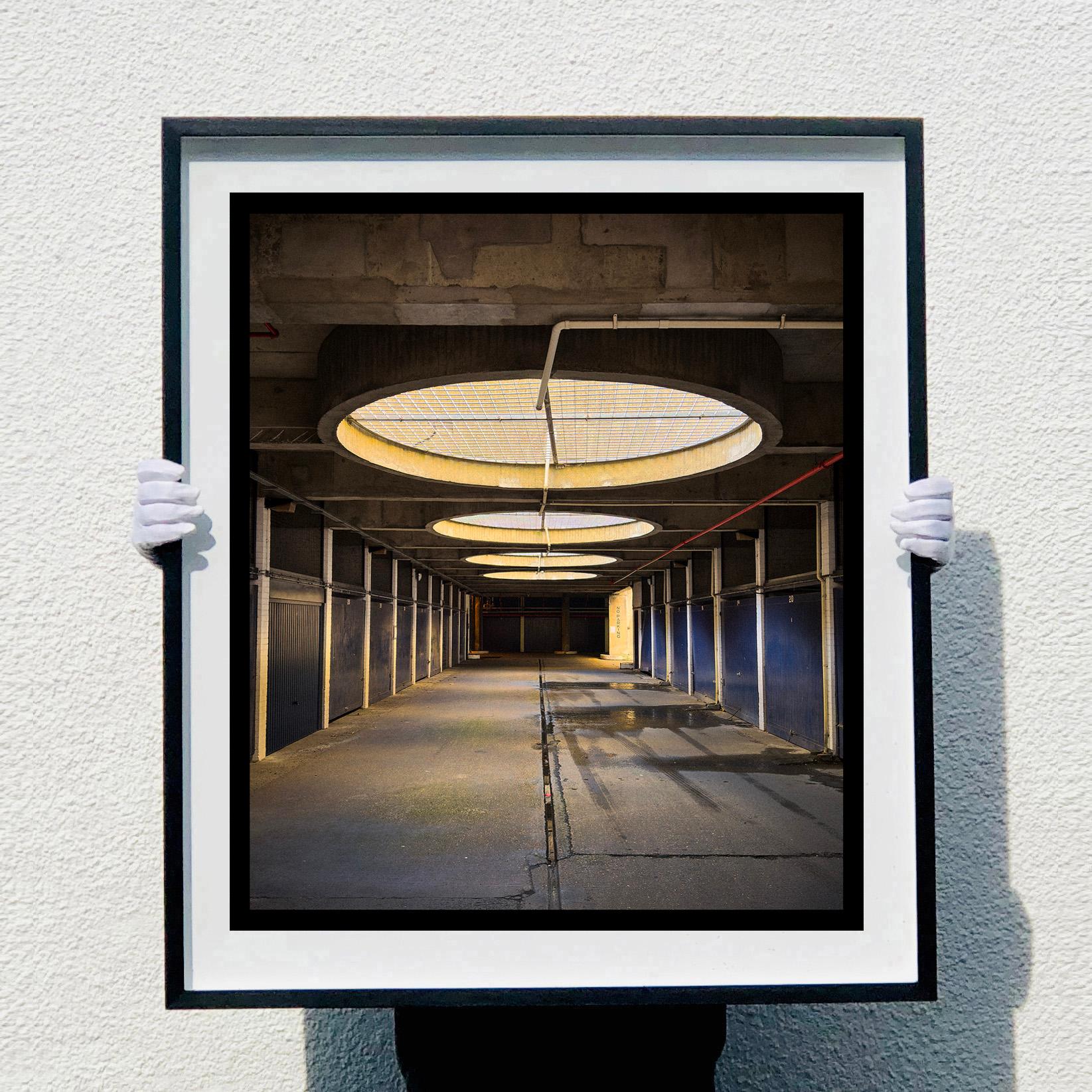 No Parking, Foto der Stadtarchitektur aus Richard Heeps Serie A Short History of London. Die strenge brutalistische Architektur hat einen Sinn für Schönheit, denn die hypnotische Symmetrie zieht den Blick durch das Bild.

Dieses Kunstwerk ist eine