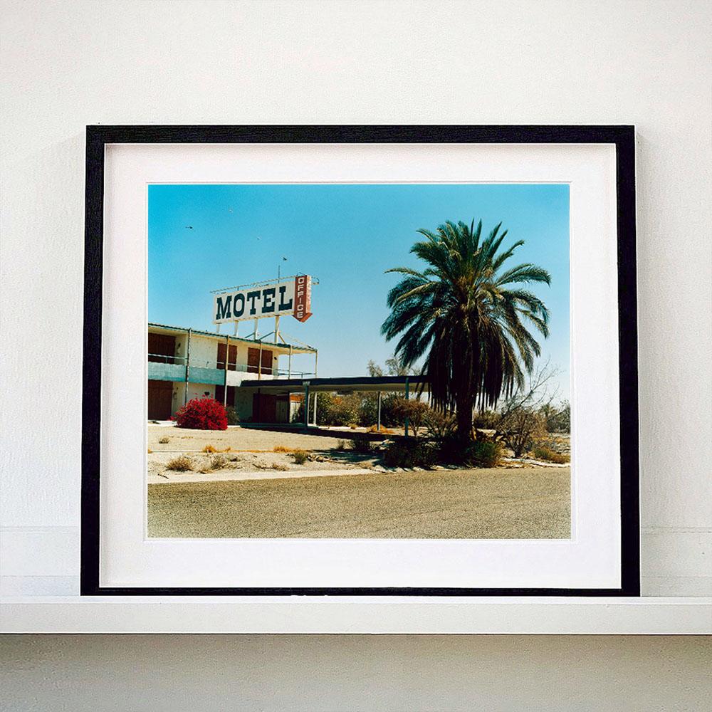 North Shore Motel, photography by Richard Heeps captured in the Salton Sea, California. A classic American faded roadside Motel, the mid-century architecture stands against with blue sky with a bushy palm tree. 

This artwork is a limited edition of