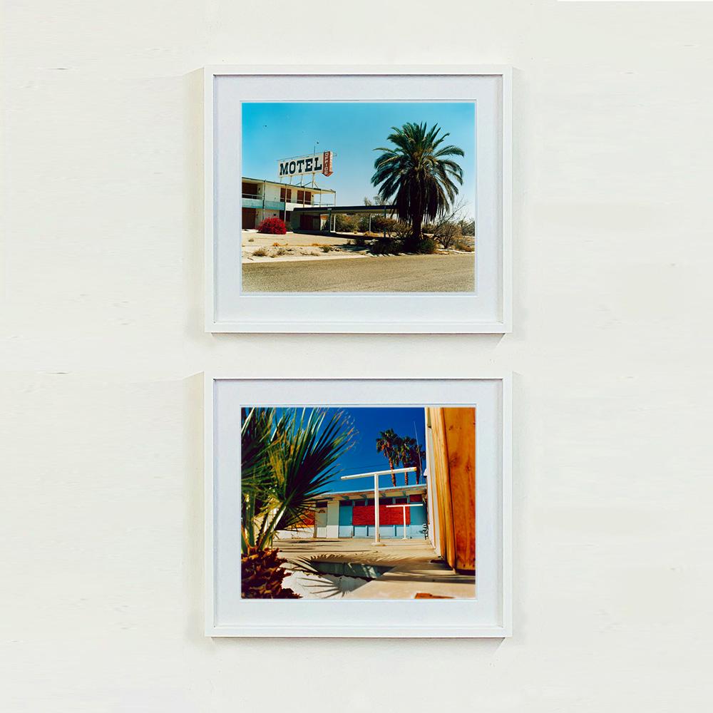 North Shore Motel, Fotografie von Richard Heeps, aufgenommen am Salton Sea, Kalifornien. Ein klassisches amerikanisches Motel am Straßenrand, dessen Architektur aus der Mitte des Jahrhunderts sich vor blauem Himmel mit einer buschigen Palme abhebt.