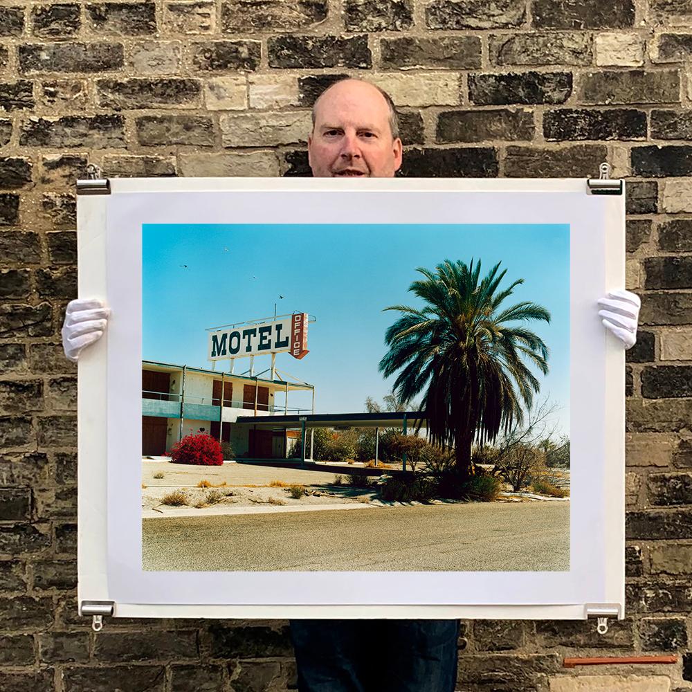 North Shore Motel, photography by Richard Heeps captured in the Salton Sea, California. A classic American faded roadside Motel, the mid-century architecture stands against with blue sky with a bushy palm tree. 

This artwork is a limited edition of