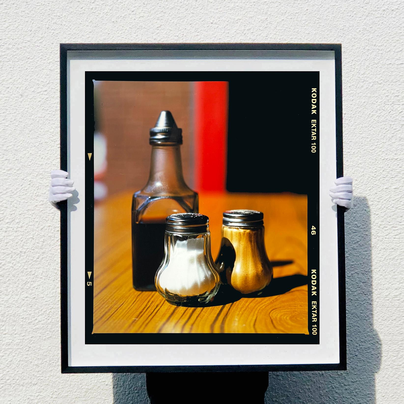 Sale, pepe e aceto compongono questa fotografia di still life, scattata in un caffè di Clacton-on-Sea, al mare, nell'anno della grande vacanza britannica. È stata scattata nel vero stile di Richard Heeps, mostrando la bellezza e l'interesse per