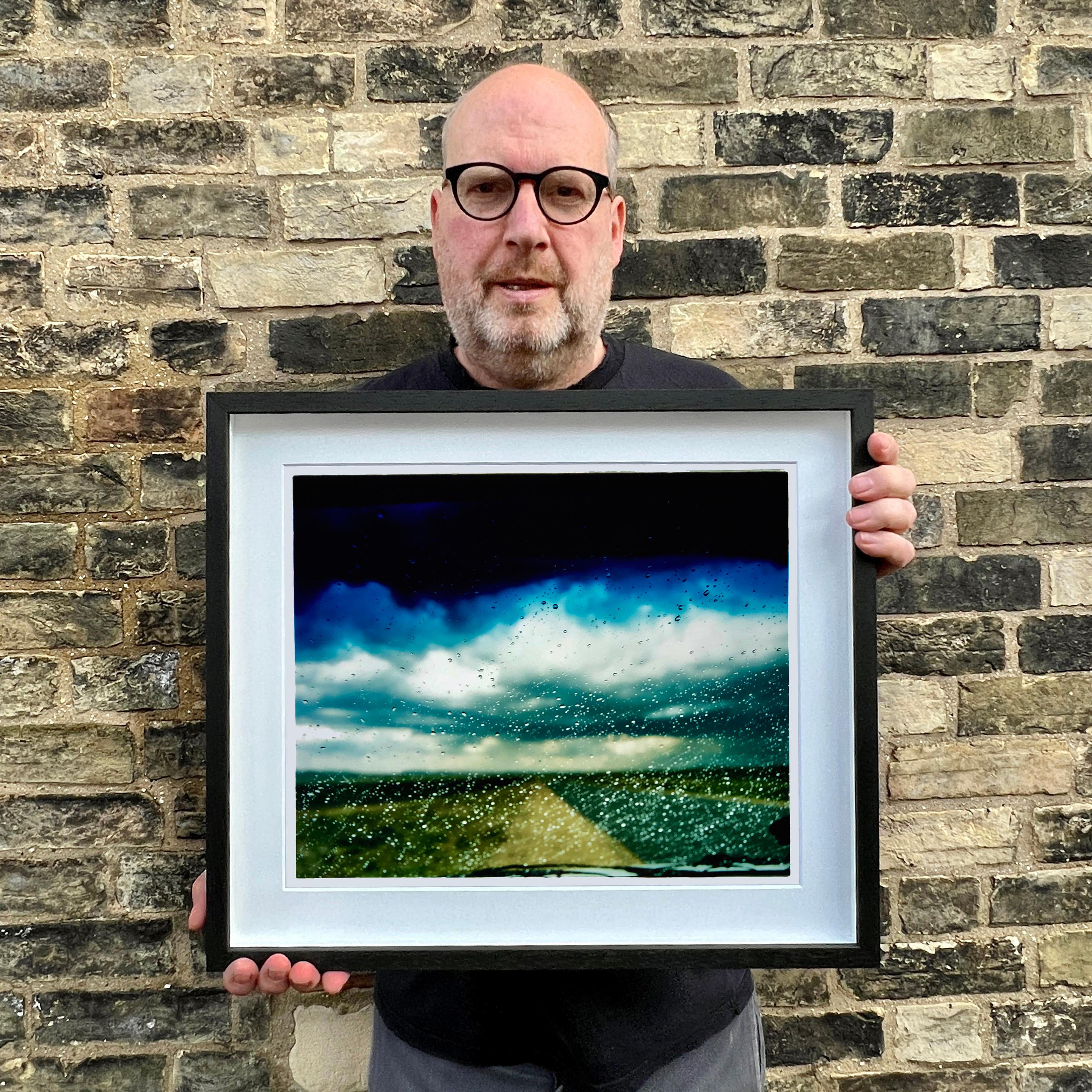 Ventana tintada, la lluvia cae sobre la ventanilla de un coche en una carretera sudafricana, fotografía de paisaje de la serie de Richard Heeps, La nueva linterna.
La obra de Richard Heeps te lleva de viaje, la carretera es un tema recurrente, a