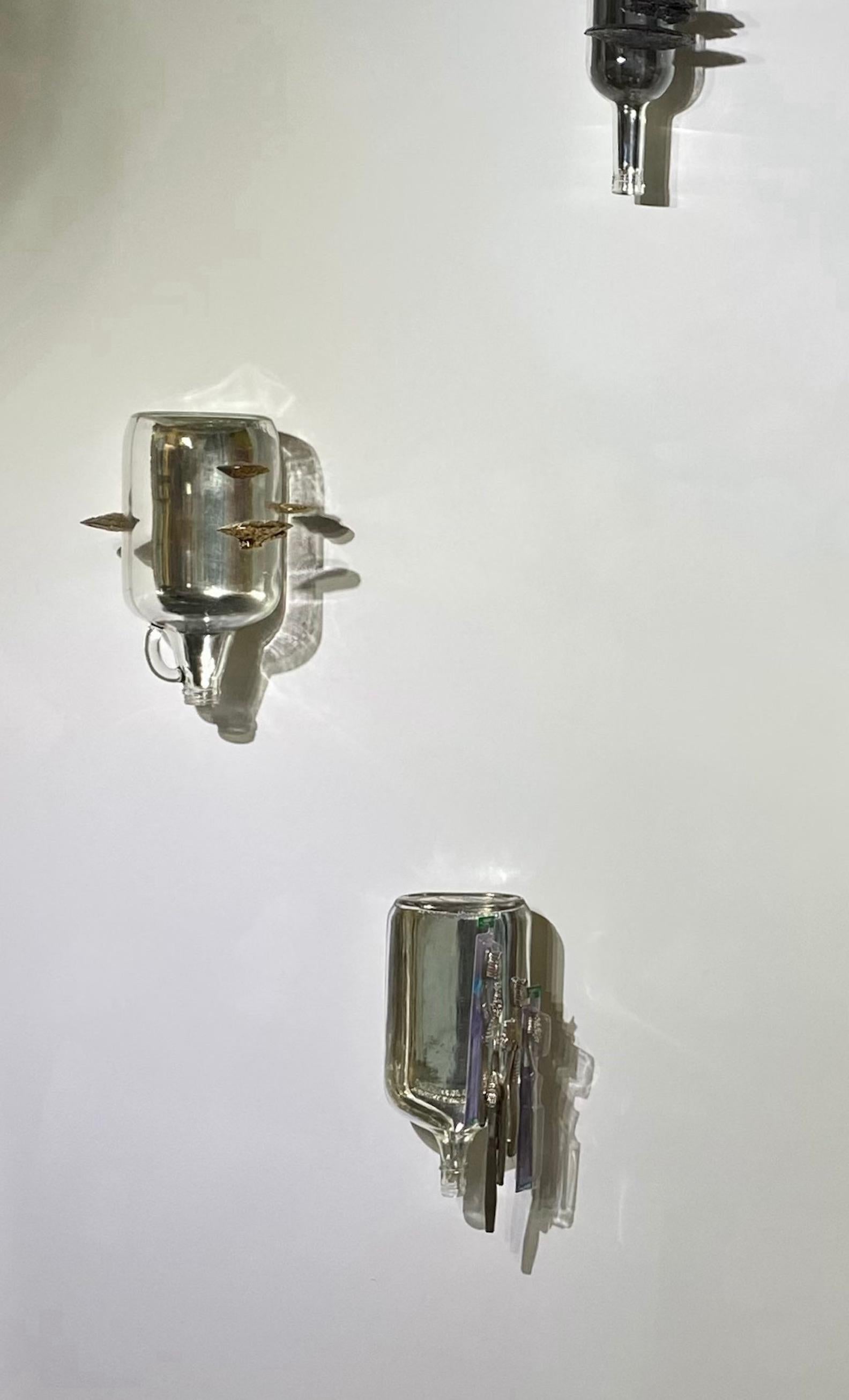 In this wall-mounted sculpture, copper and brass plated bracket, or shelf fungi line the sides of a glass jug with a handle on the spout hanging upside down, mirrored with white gold leaf on half of the inside creating a reflective inner side