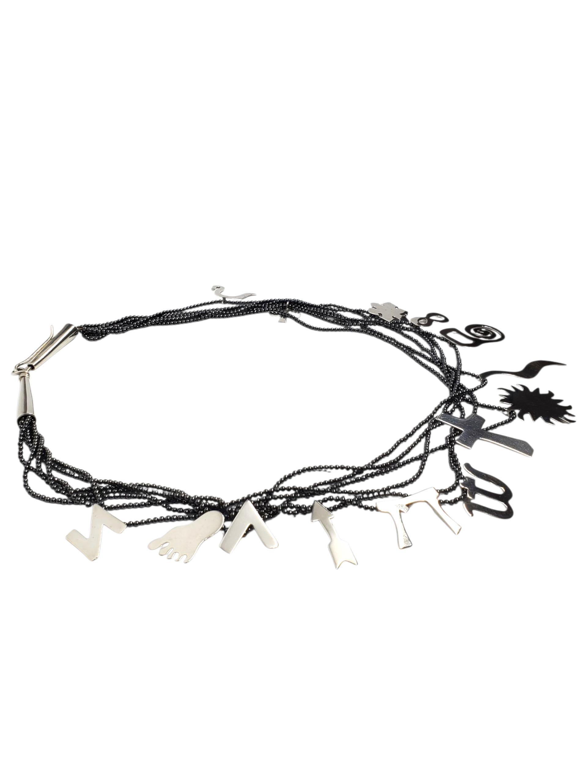 A. Richard Silver Collana con ciondolo multi charme in perline in argento sterling -

Questa collana di perline in argento sterling, realizzata a mano da Richard Lindsay, presenta una serie di charme simbolici infilati in 6 fili con chiusura a