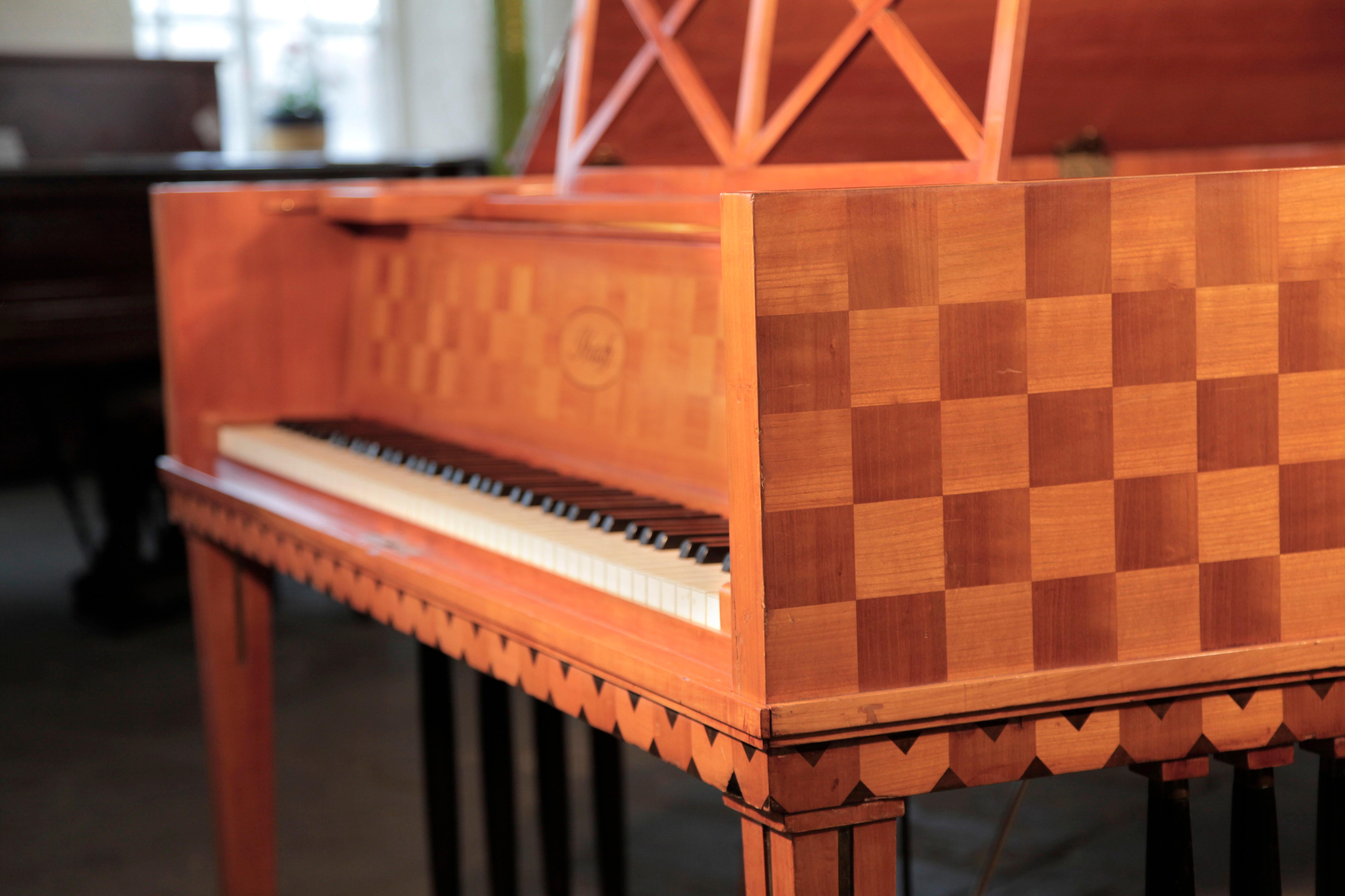 Restored, 1907 Ibach Model 2 grand piano with a cherry case in a checkerboard design and inlaid, contrasting squares on the piano lid. Piano music desk is in an openwork dual criss-cross design. Piano has gate legs with four contrasting black