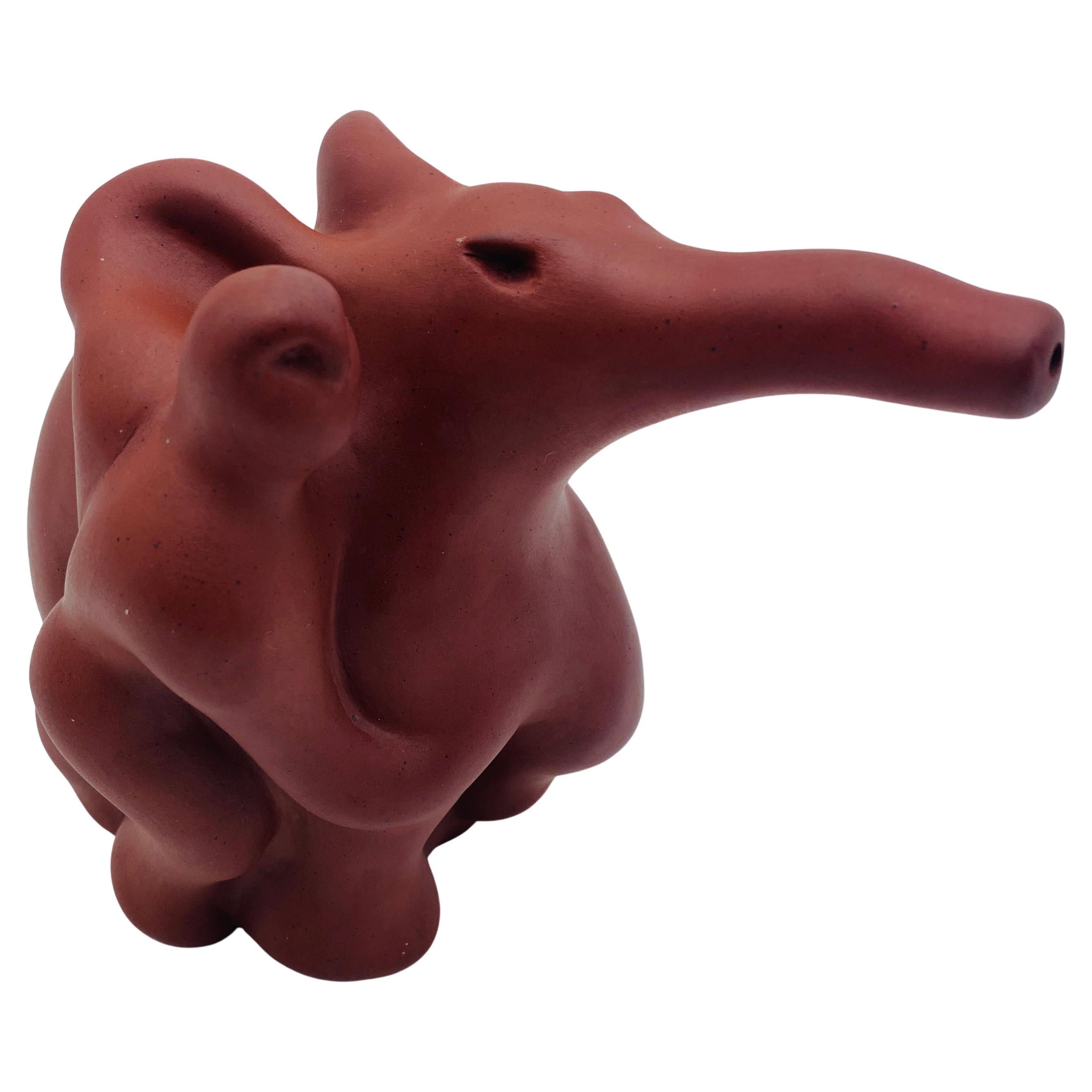 A iron red clay studio teapot made by artist Richard Swanson. The teapot depicts an elephant rider with a removable lid. The underside is signed Swanson edition. 