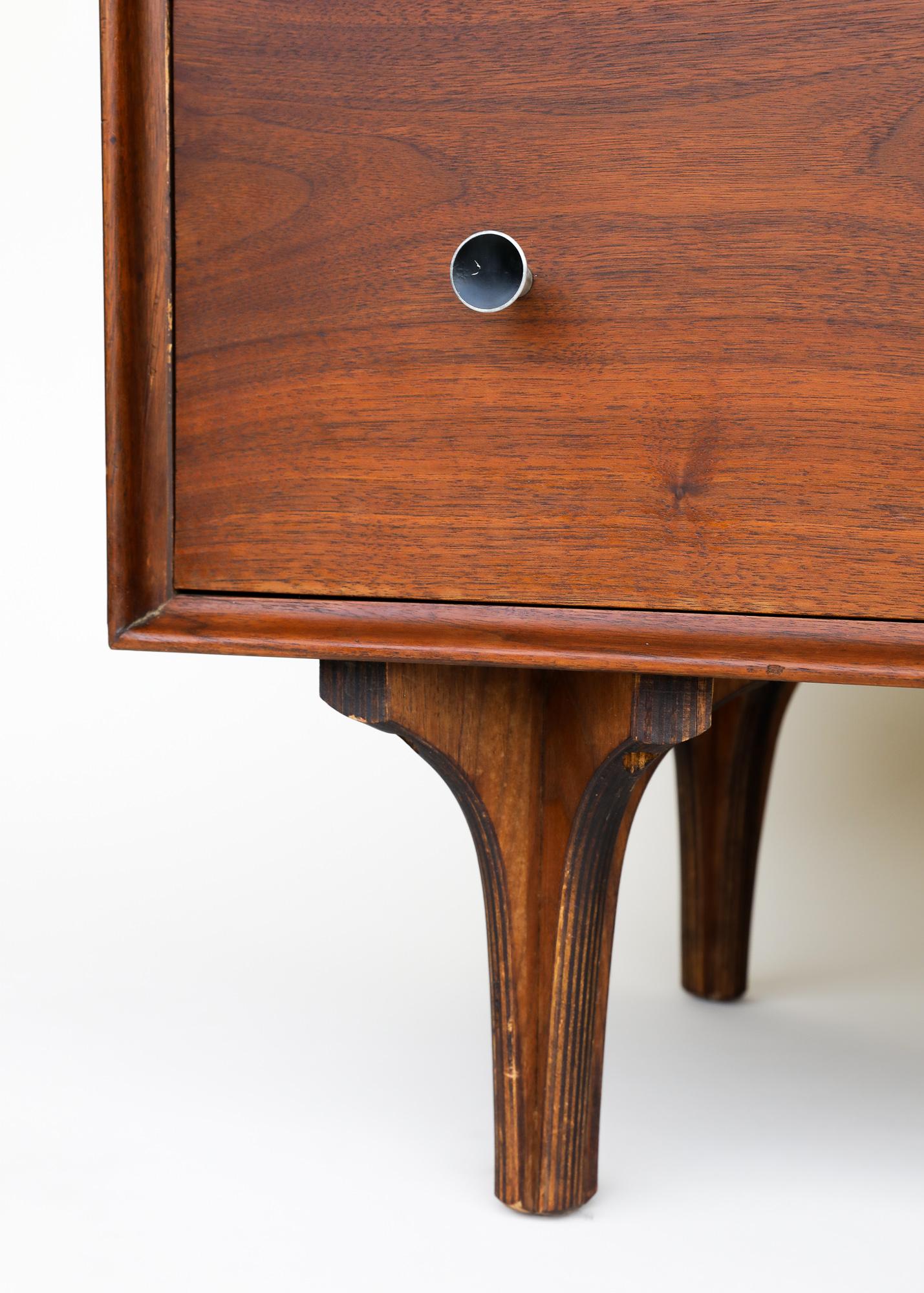 This is a beautiful mid-century modern dresser designed by Robert Thompson for Glenn of California in the United States circa 1950's. This spacious vintage dresser features a sturdy walnut wood frame with sculptural legs indicative of Glenn of