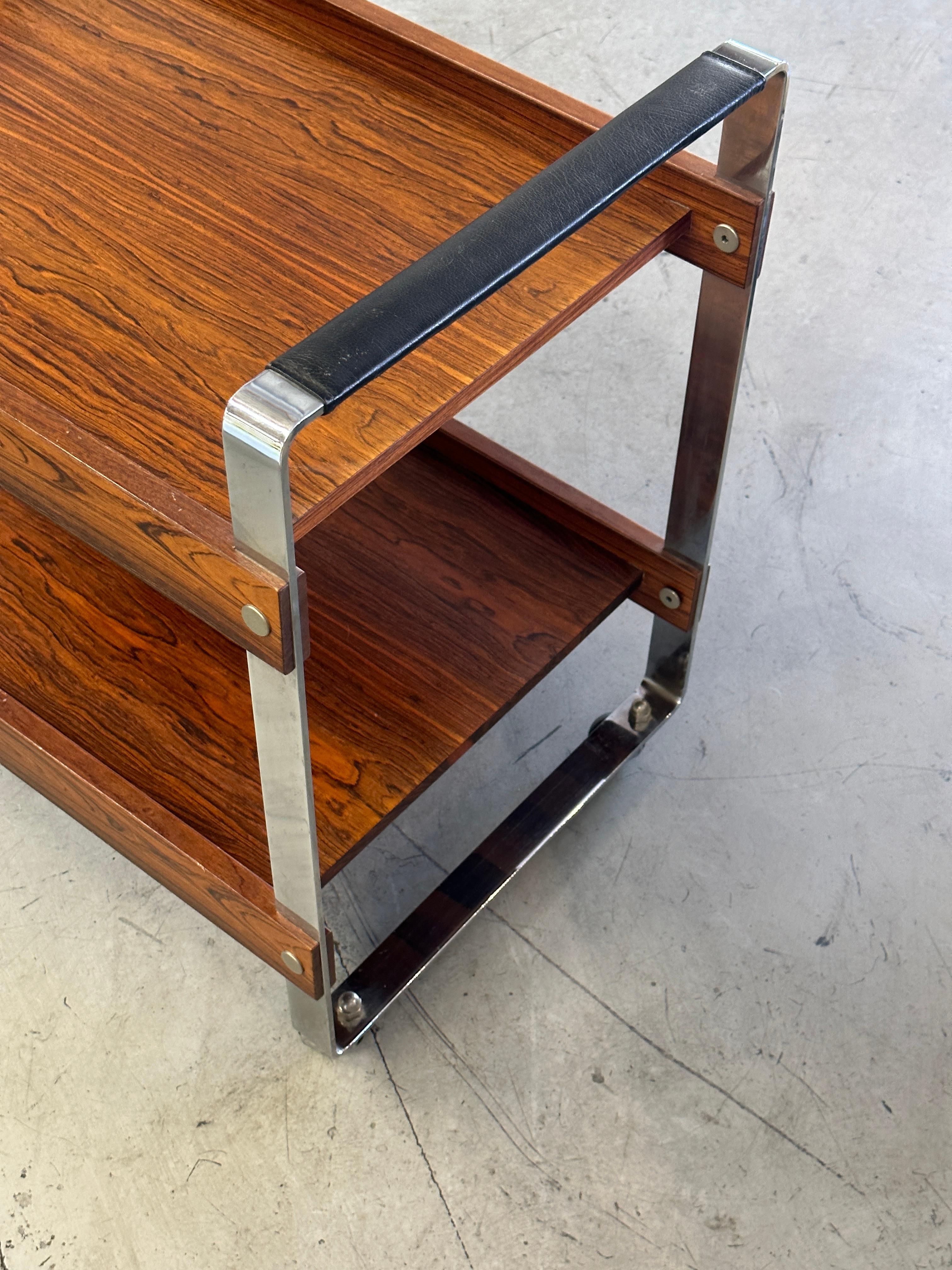 A pretty rosewood and chrome designed by Richard Young for Merrow Associates in the 1960s. The bar is on 4 castors and glides smoothly. Beautiful graining to the wood. In good age appropriate condition although there is some minor lifting to the