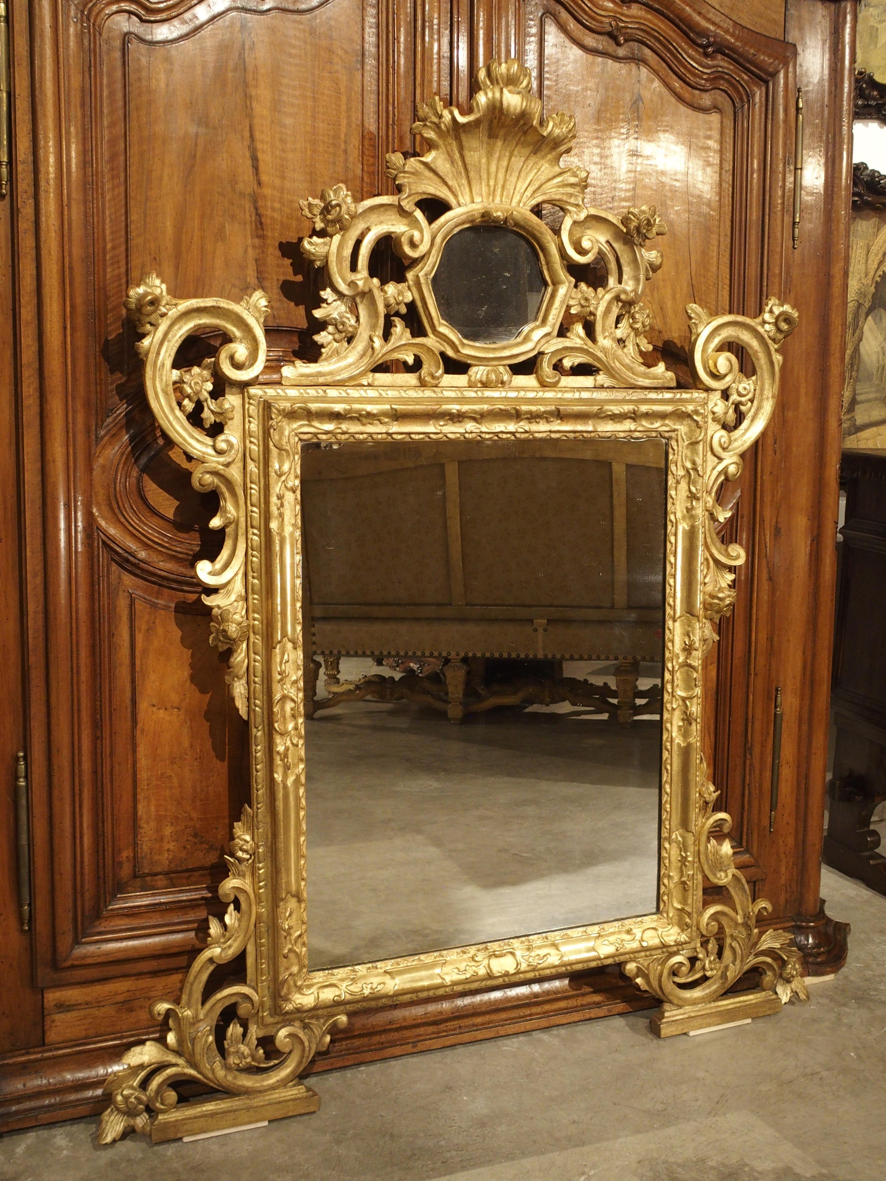 From Italy, circa 1850, this richly carved Venetian giltwood mirror features a small roughly circular mirror inset in an elaborate crown

A stylized shell with acanthus tips emanates from the top of the small mirror. This upper mirror is
