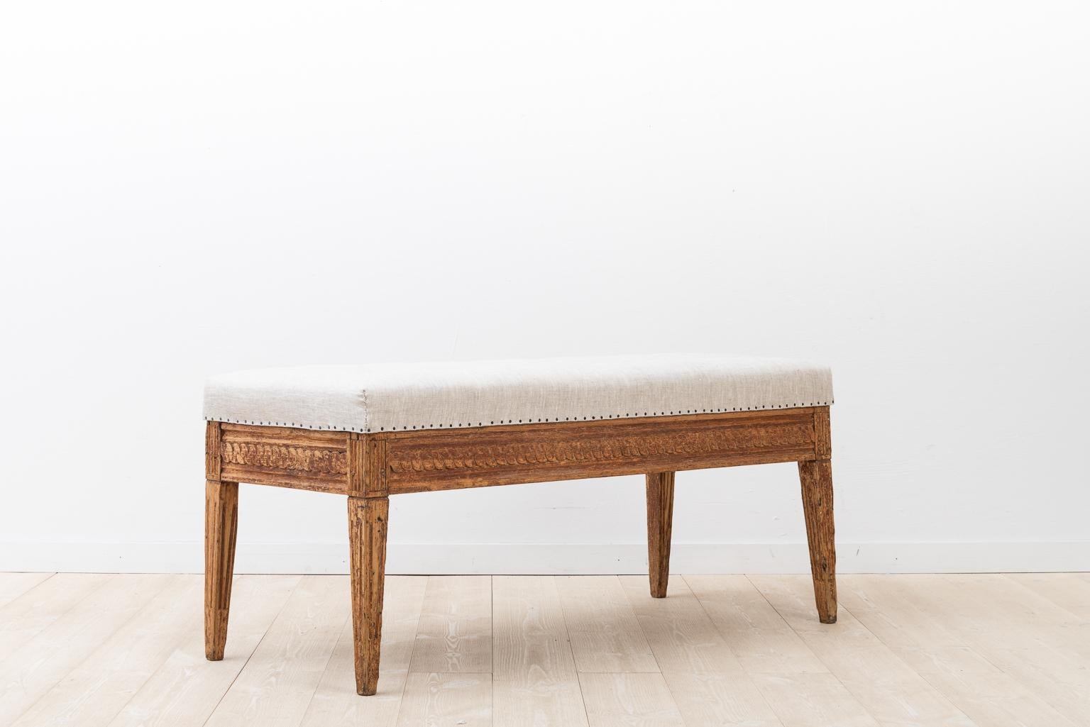 Gustavian bench manufactured in Sweden during the 1790s. Remaining traces of the original paint. Richly decorated with Gustavian styled wooden carvings. The seat has been renovated and dressed with linen fabric.
   