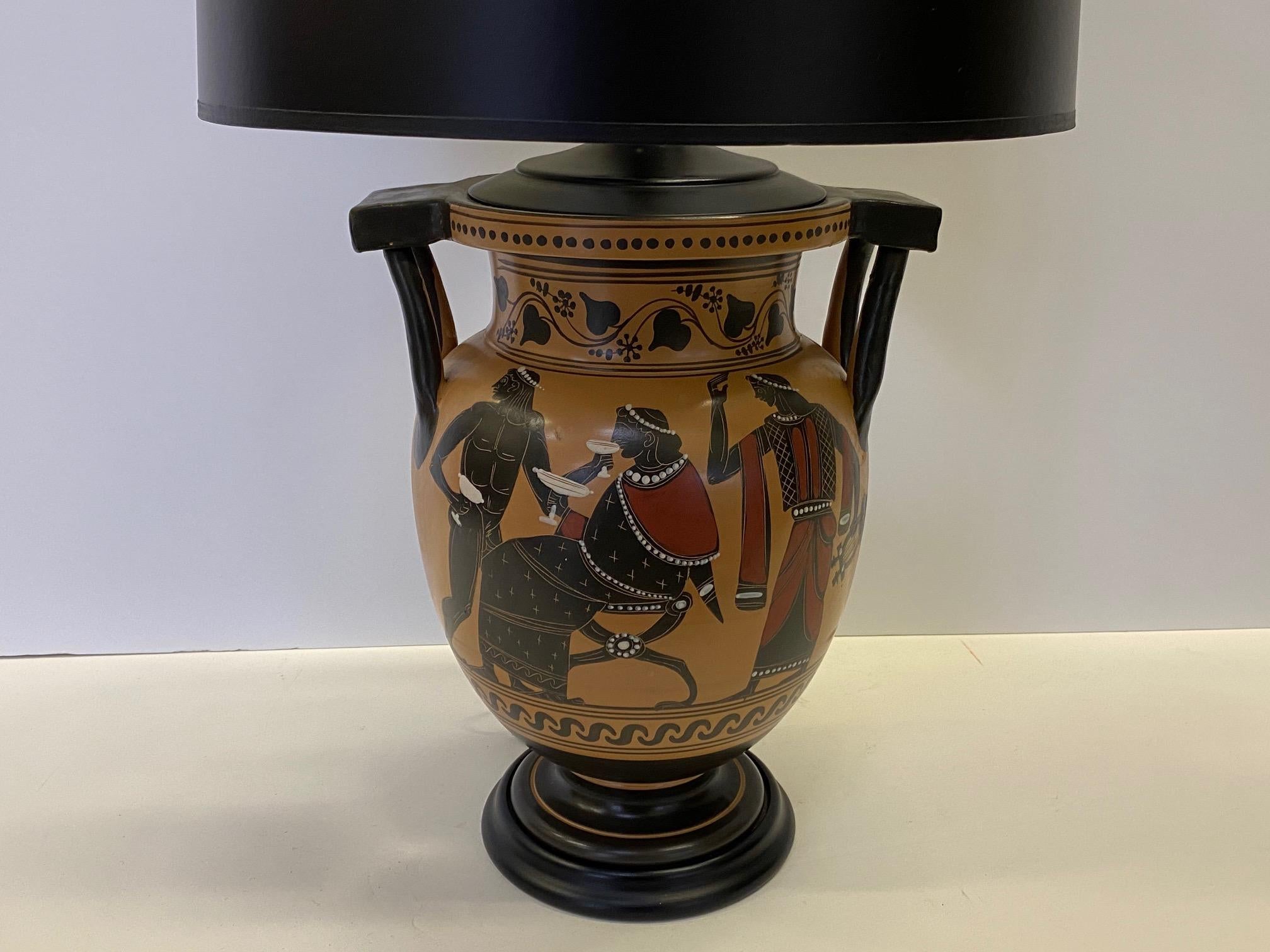 A gorgeous classical Greek style vase having hand painted warm gold background with black and red oxide ancient figures that has been transformed into a striking table lamp with black shade.