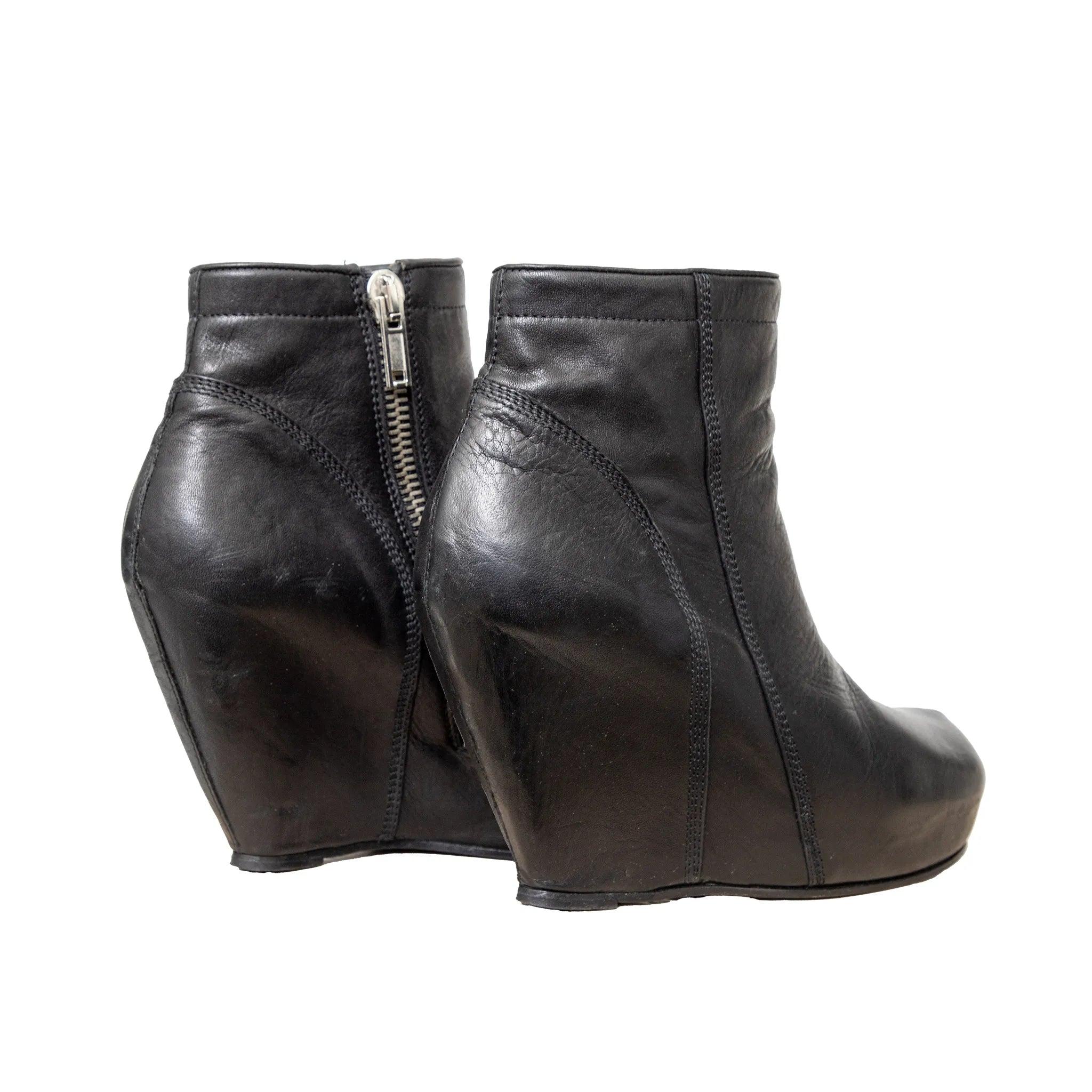 Icónicos botines Rick Owens de piel negra con tacón de cuña esculpido, puntera cuadrada, cremallera lateral expuesta y plataforma oculta. Silueta vanguardista característica.
 Inclusión: caja.
 Observaciones: presenta signos de desgaste. 
 Material: