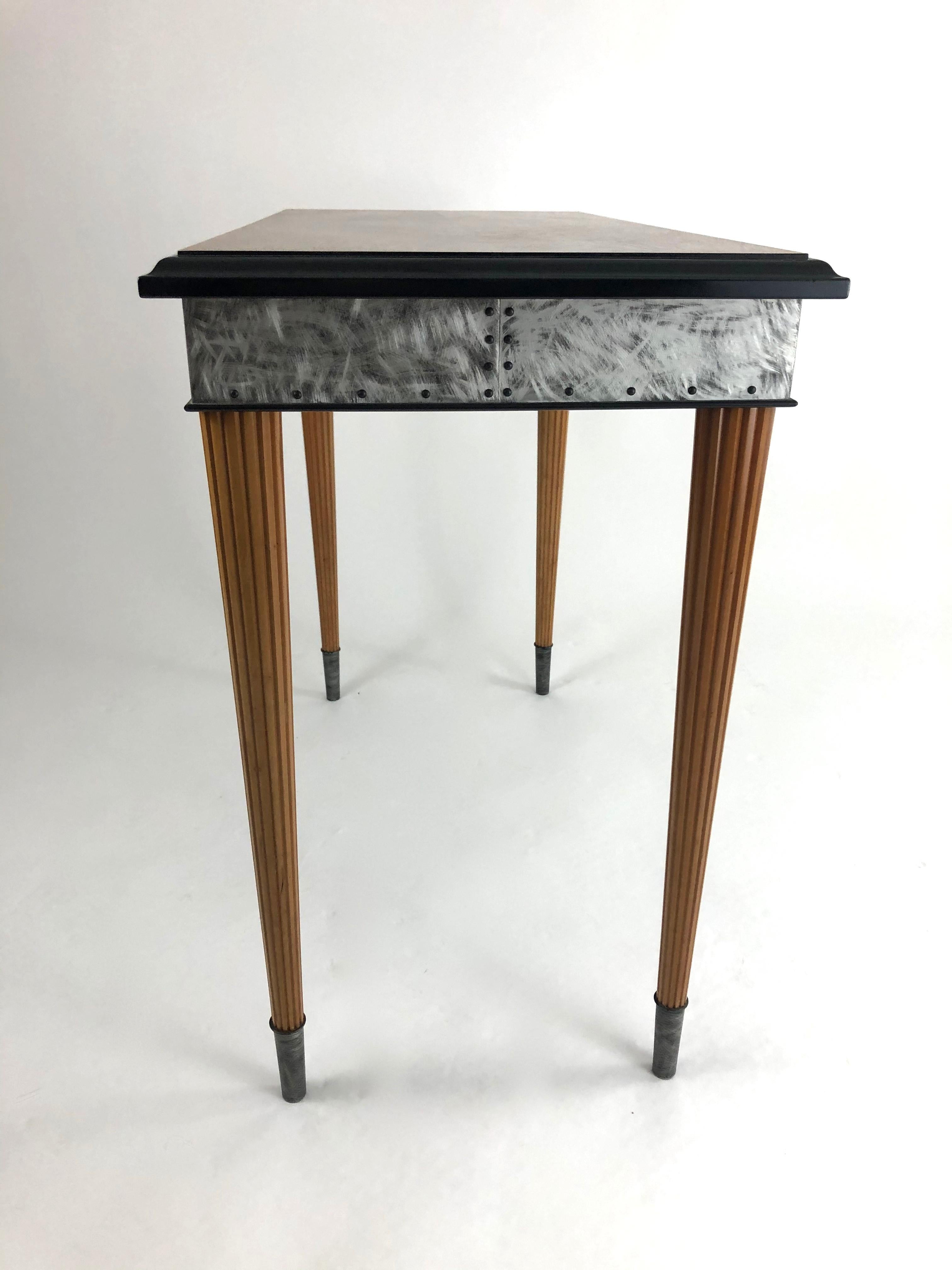 A fine quality studio furniture console table by American artist, Rick Wrigley (please see biography below). The rectangular top is in richly figured amboyna veneer surrounded by an ebonized cherry ogee moulded edge, over a patinated aluminum frieze