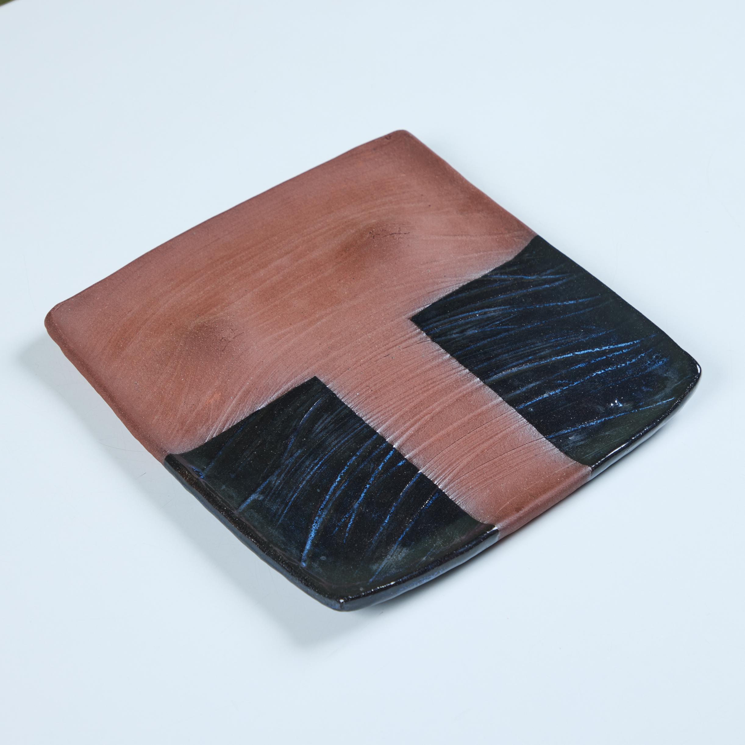 Ceramic plate by California artist, Rick Yoshimoto. Rick has been creating pieces out of Northern California since the late 1970s. This piece features a square shape with slightly turned up edges. The plate has two circular indentations on one side