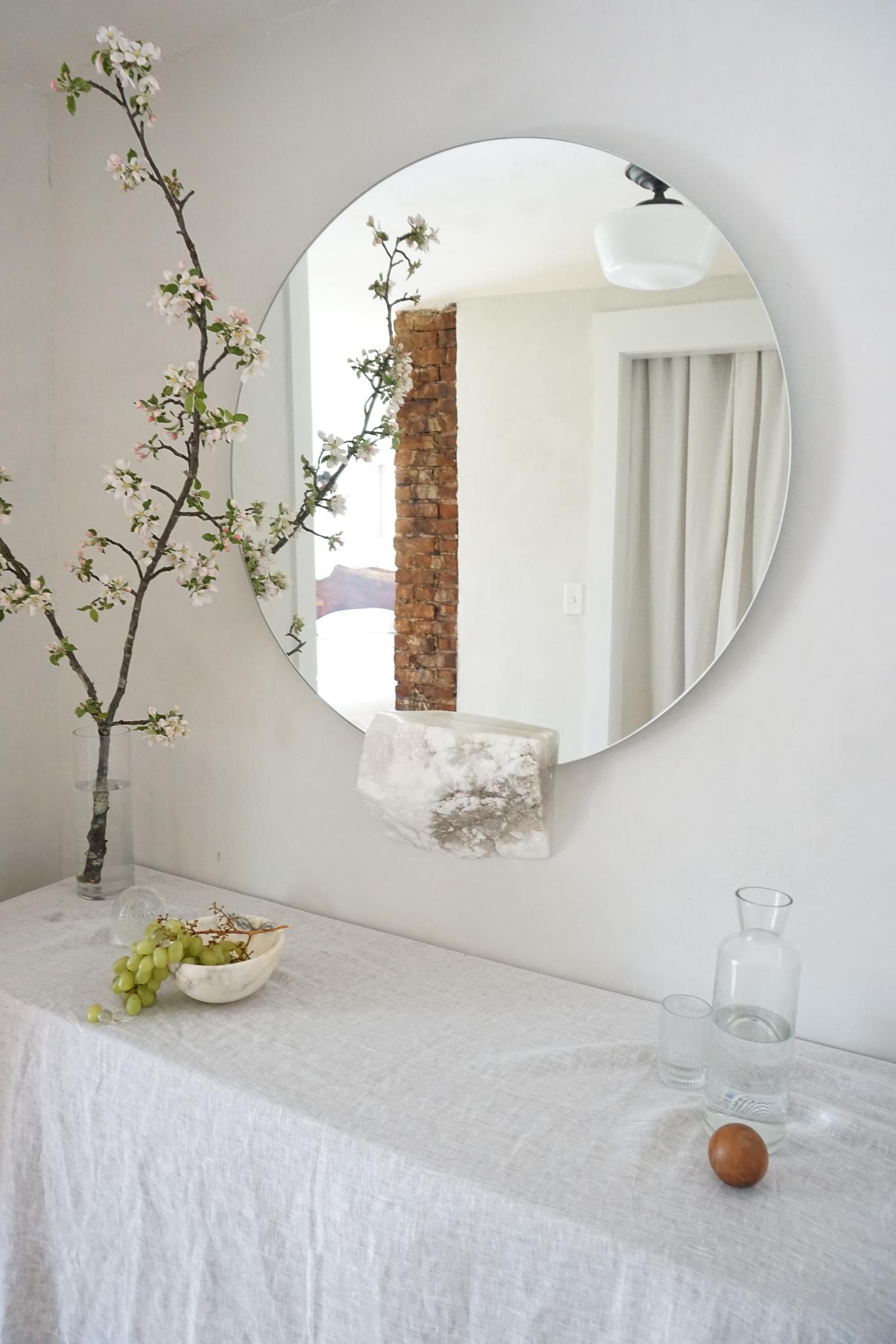 Ridge mirror by Swell Studio
Dimensions: Mirror: D82 cm. Stone: D 11 x W 81 x H 21 cm 
Material: Alabaster, (mirror available in smoke, bronze, antiqued & peach)


A round wall mirror, supported by a white alabaster cut off rests in contoured