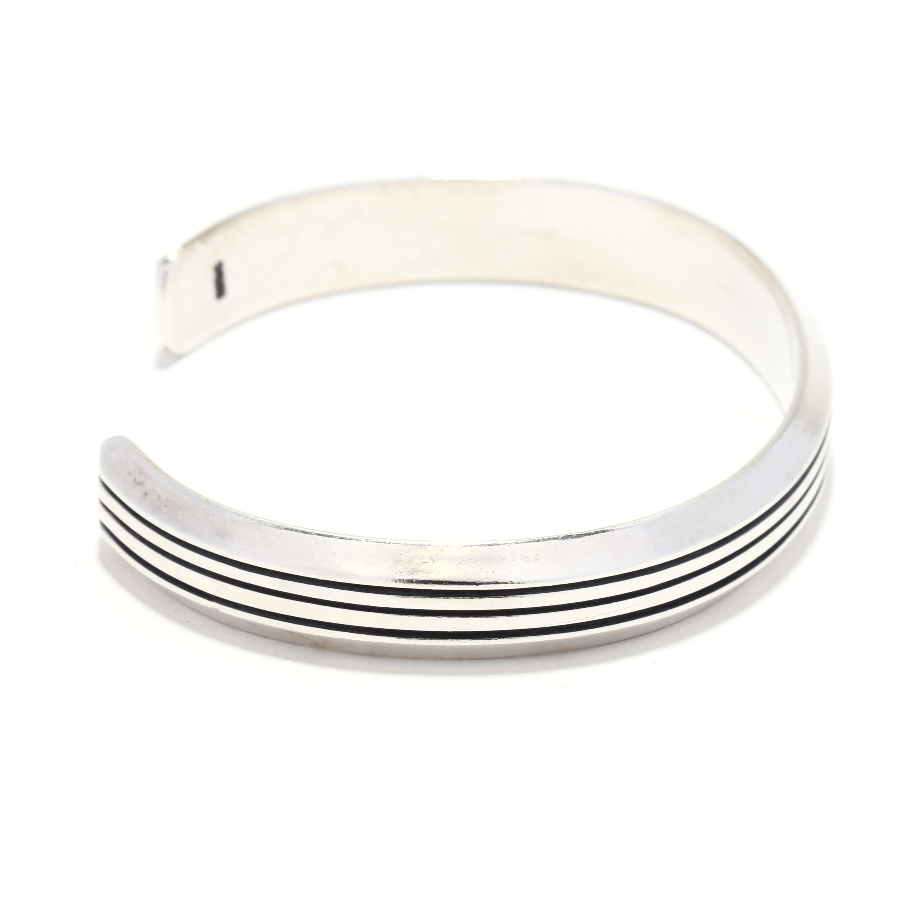 A sterling silver ridged cuff bracelet. This simple silver cuff bracelet features a band of incised engraved lines and a beveled edge. It is stamped 925. 

Length: 6.5 inch interior circumference with 1 inch opening

Width: 5/16 inch

Weight: 16.7