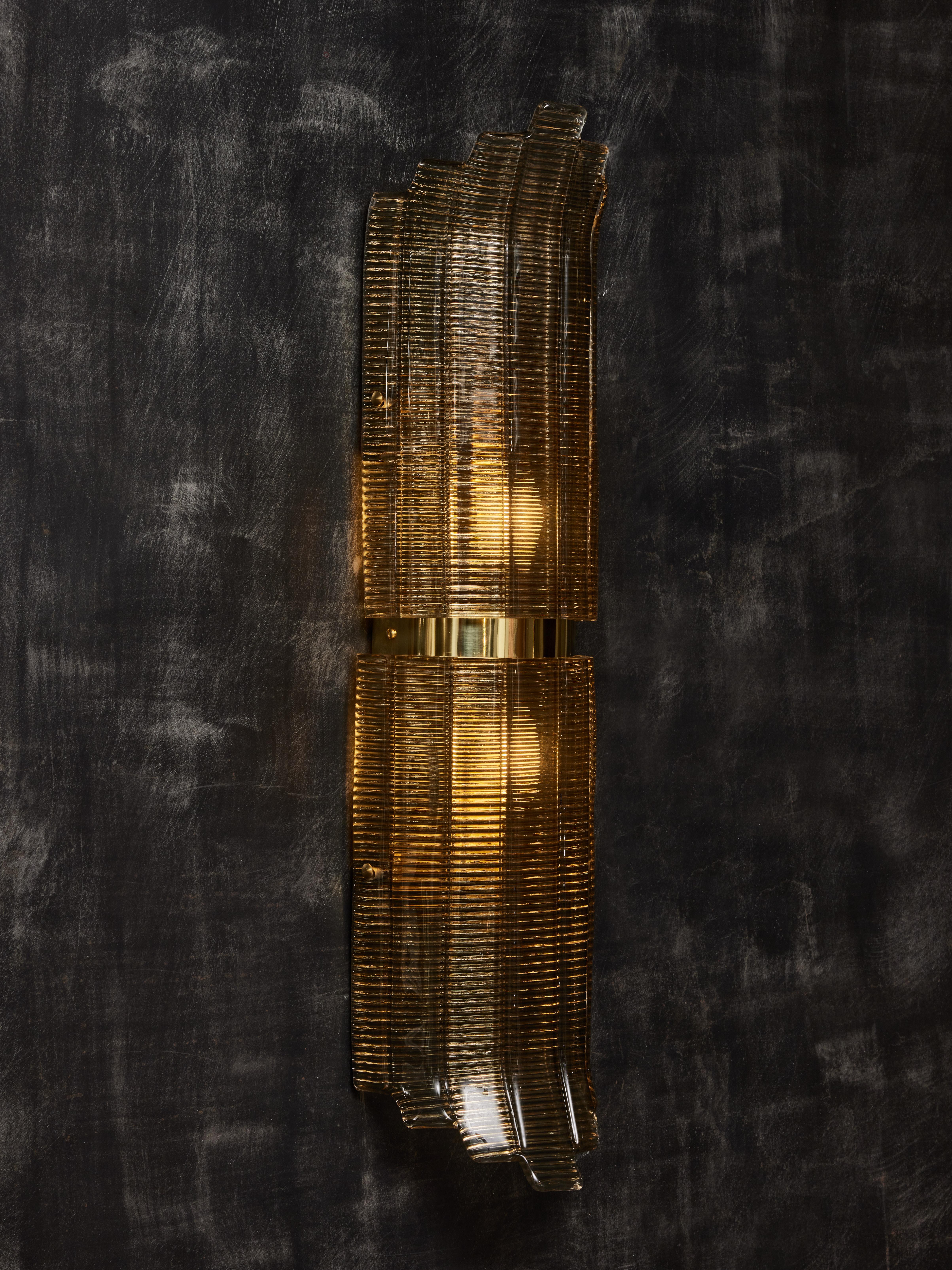 Wall sconces made of two elements of Murano glass, ridged and smoked, put together with a polished brass central band. 
Two lights per sconce.