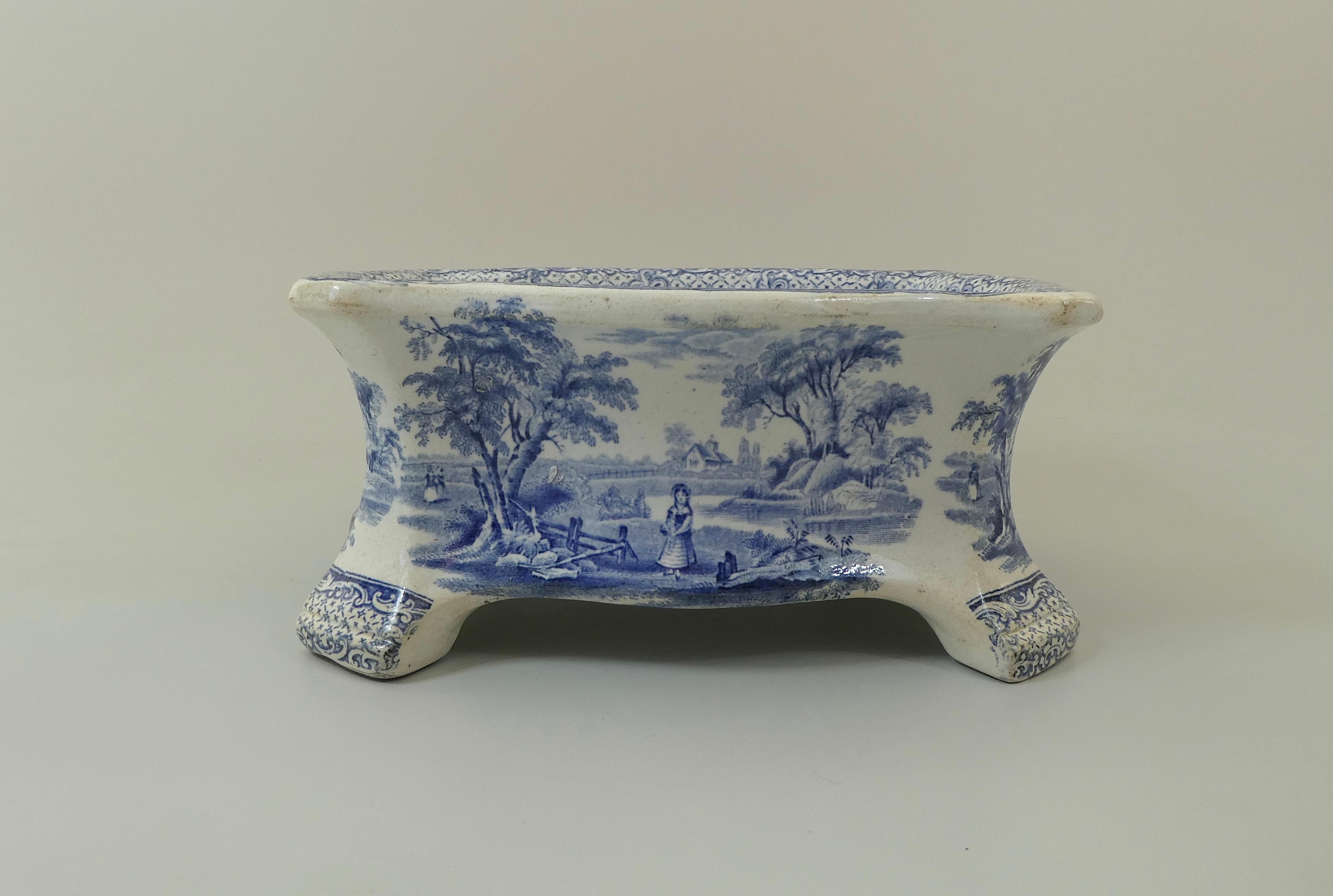 A rare Ridgway pottery dog bowl, circa 1840. The shaped dog bowl, set upon four moulded feet, and printed in underglaze blue, with figures in a rural landscape. within a swag and scroll border. The exterior printed with the same scene.
Printed mark