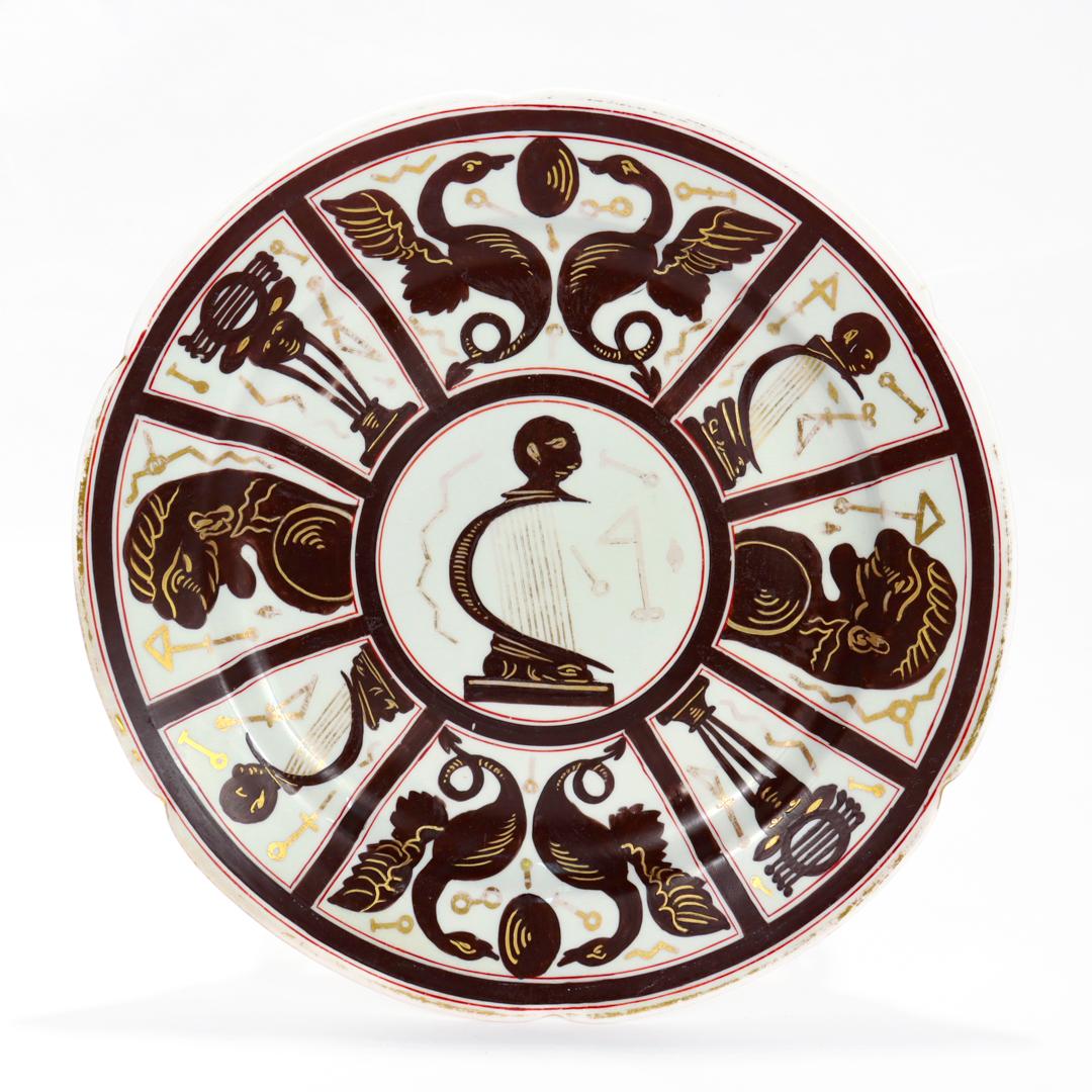 A fine English bone china dinner sized plate.

By Ridgway.

In the No. 135 'Egyptomania' pattern.

With black and gold Egyptian inspired decoration with red accents on a white ground. 

The rim is scalloped with gilding.

Marked N.135 to the