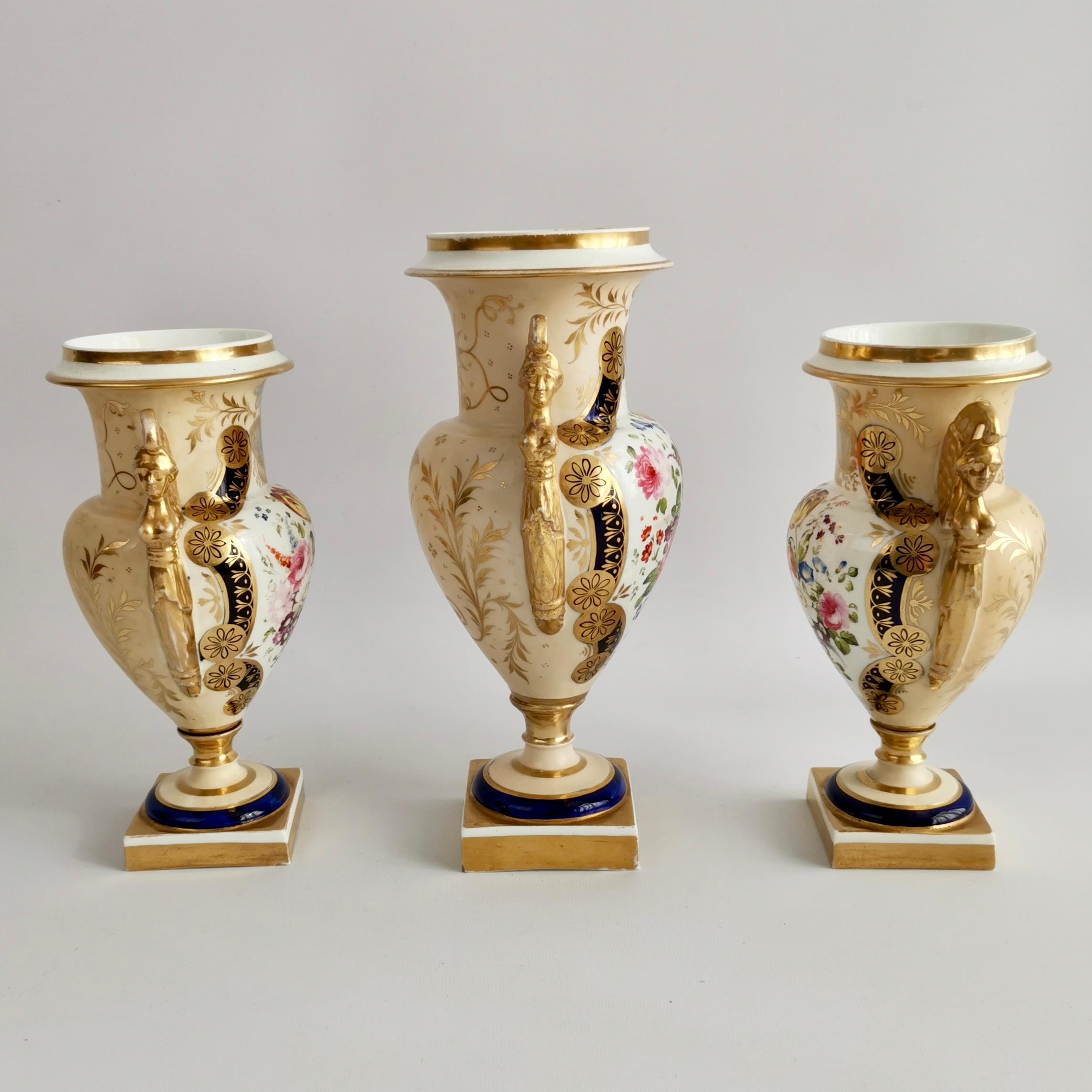 Es handelt sich um eine spektakuläre Garnitur aus drei Vasen, die zwischen 1810 und 1815 in einer englischen Fabrik hergestellt wurde. Die Vasen sind im französischen Empire-Stil gefertigt, haben stark vergoldete ägyptische Karyatidengriffe,