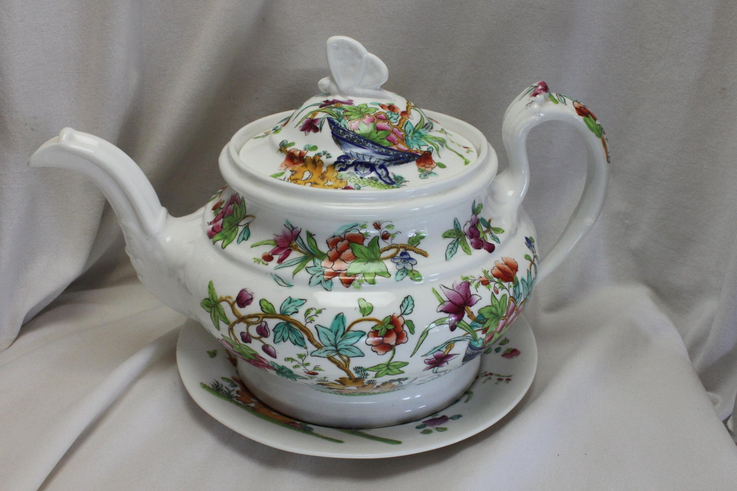This finely moulded John and William Ridgway porcelain teapot and stand is decorated with the hand coloured printed pattern 2/818, which features a large urn and scholars rocks amid floral Chinoiserie. It is unmarked, but corresponds to Plate 1798