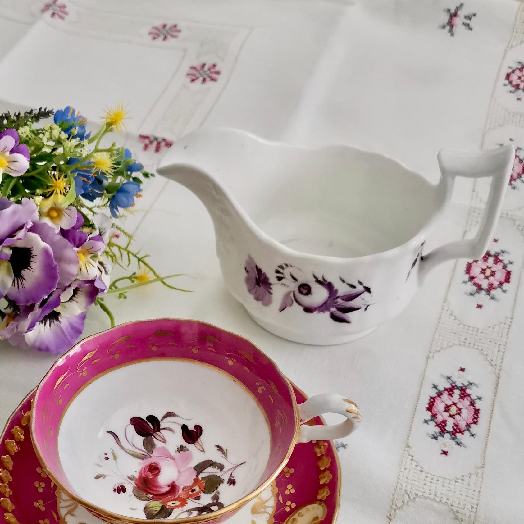 This is a charming milk jug or creamer made circa 1825 by Ridgway. The jug is decorated with simple monochrome puce / purple flowers on a white ground. The shape is typical for its time and Ridgway called it the 