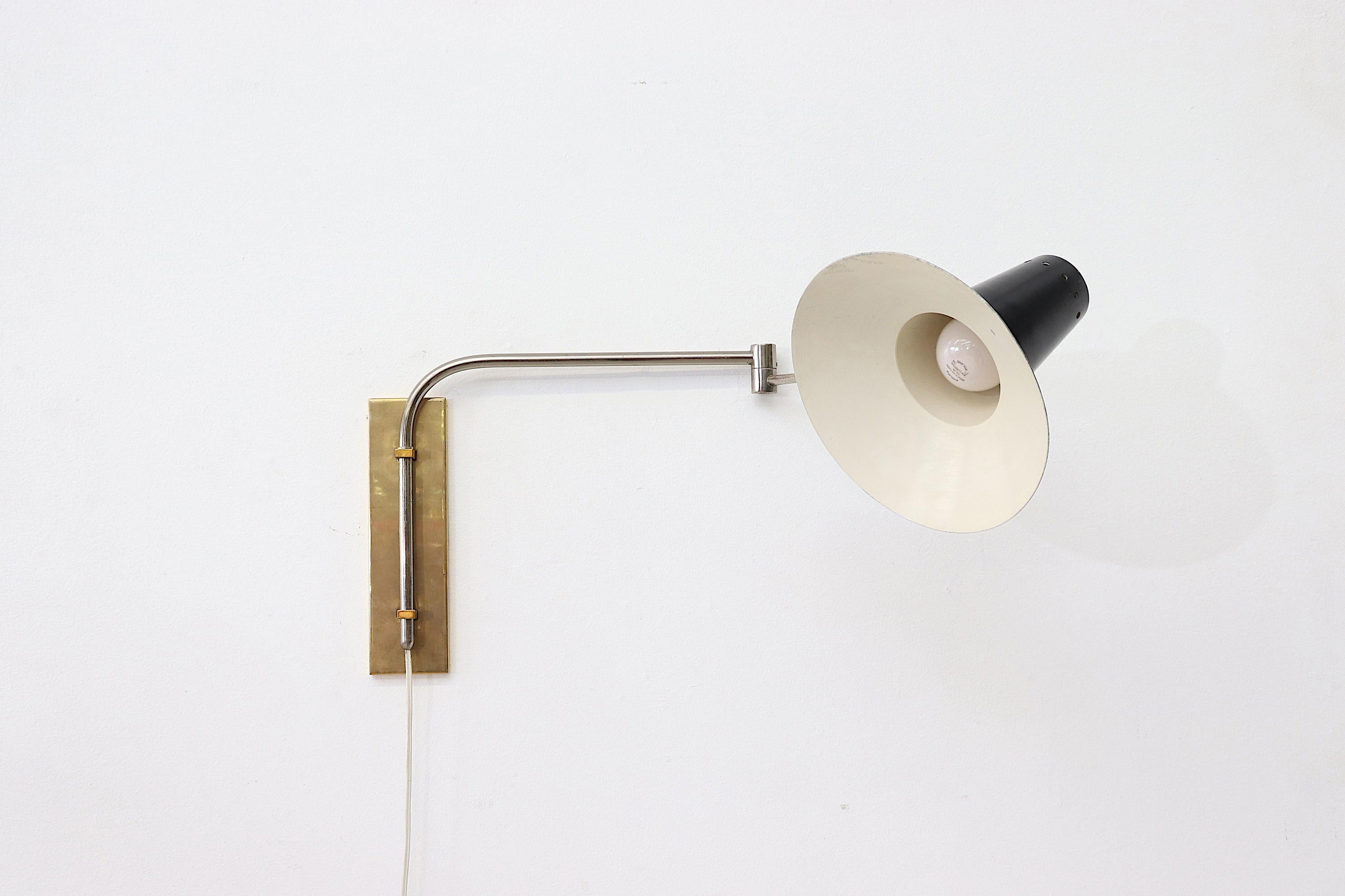Black Rietveld style industrial wall mount lamp with a chrome articulating arm and brass metal wall mount. In original condition with visible wear, minimal enamel loss. Patina is consistent with its age and usage.