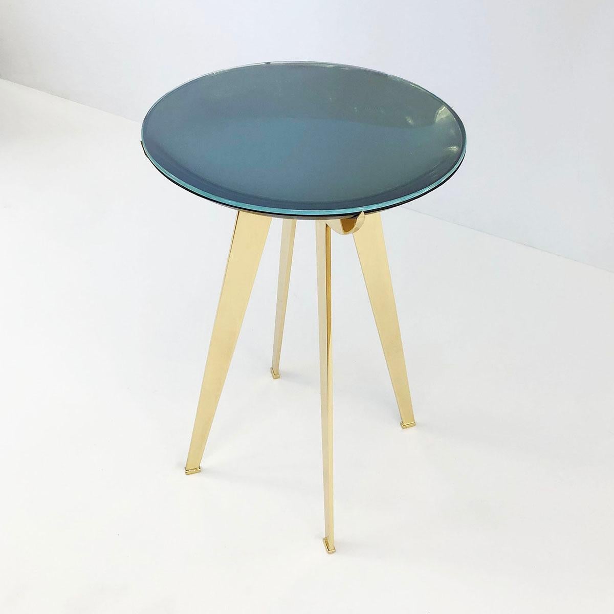 The Riflesso side table is designed around a tinted and mirrored double lens glass top which gives the piece a unique sense of depth. The brass frame with four tapered legs cradles the glass with crescent shaped supports.  Also available as a coffee