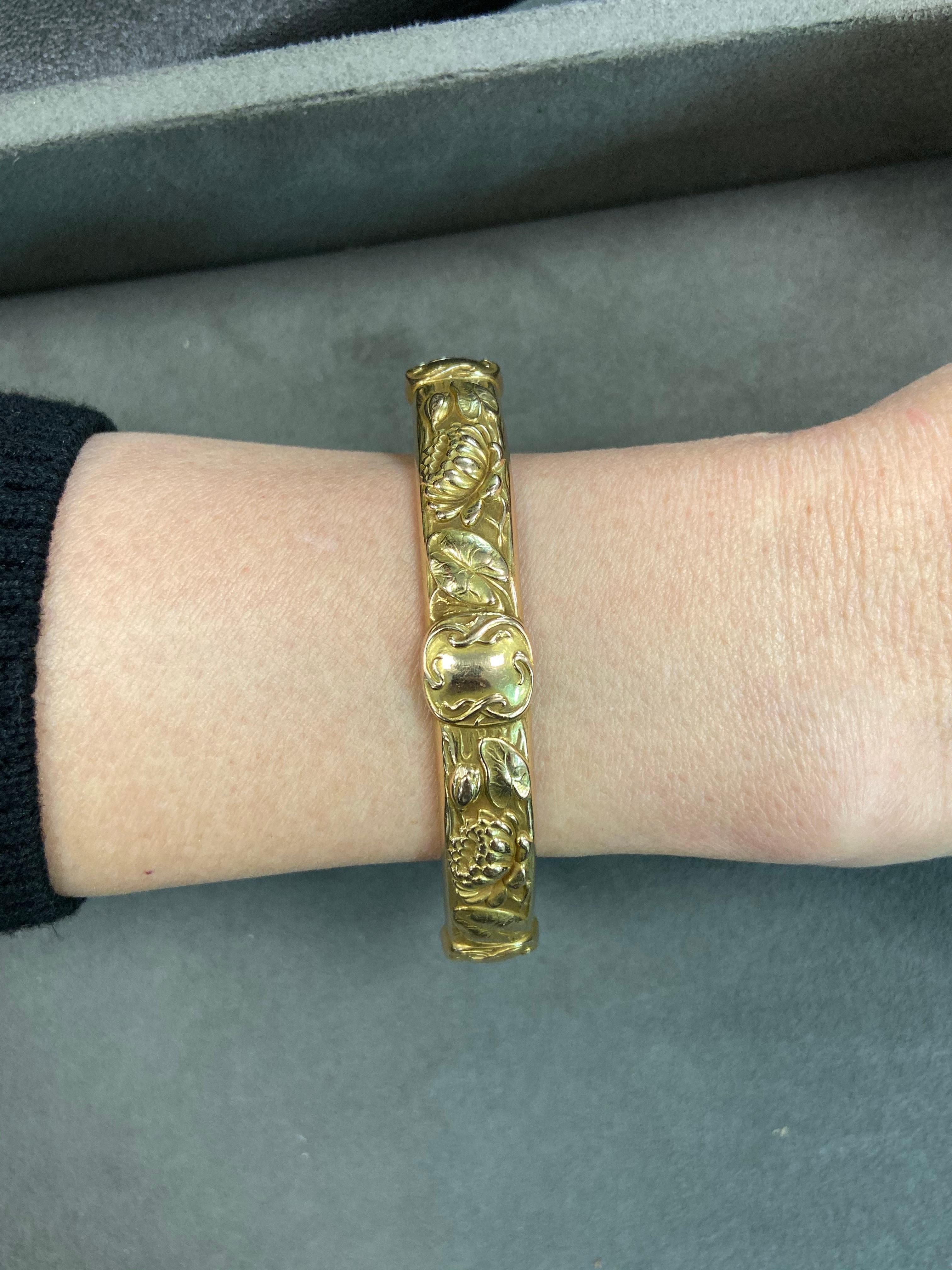 A 14 karat yellow gold hollowform bangle with lotus flower motifs bears makers marks for Riker Bros, a company based out of Newark, NJ. The bracelet is 7/16 inch wide and has an inner circumference of 7-1/2 inches.