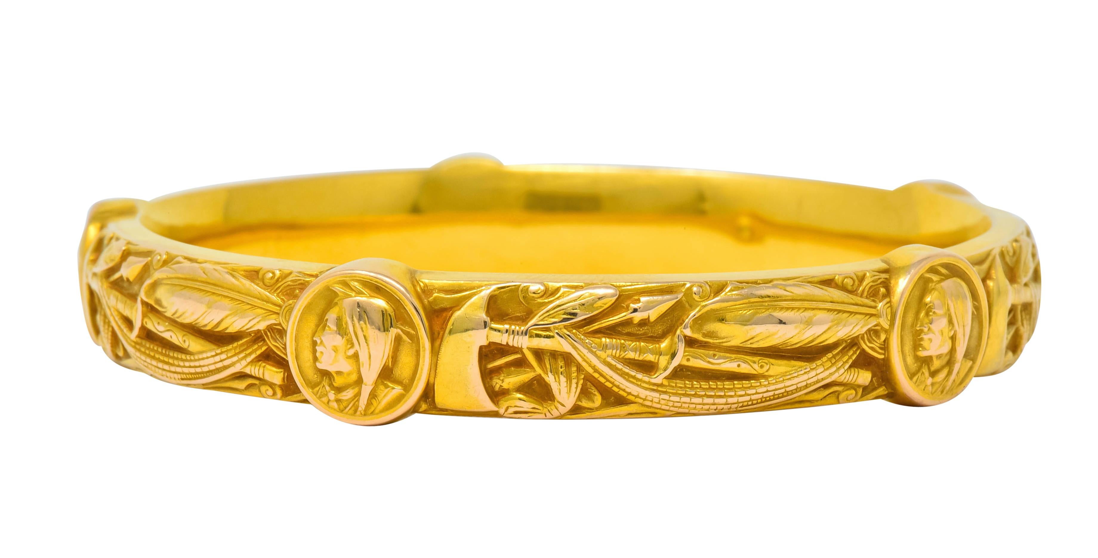 Bangle style bracelet comprised of highly rendered motifs of arrows, hatchets, feathers

With five round stations, each featuring a portrait of a Native American

With maker’s mark for Riker Brothers and stamped 14k for 14 karat gold

Circa