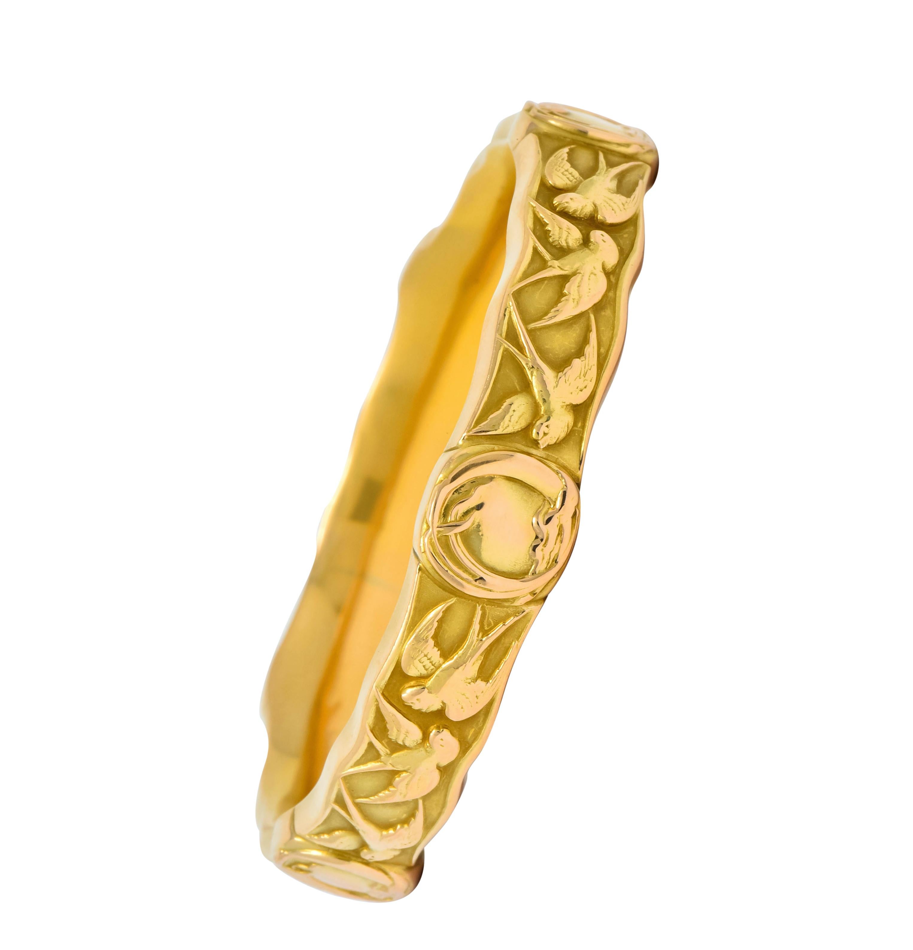 Designed as a wavy edged bangle bracelet decorated by swallow motif in three different patterns of flight

Accented by five oval stations with stylized ribbon borders

With maker’s mark for Riker Brothers and stamped 14k for 14 karat gold

Circa