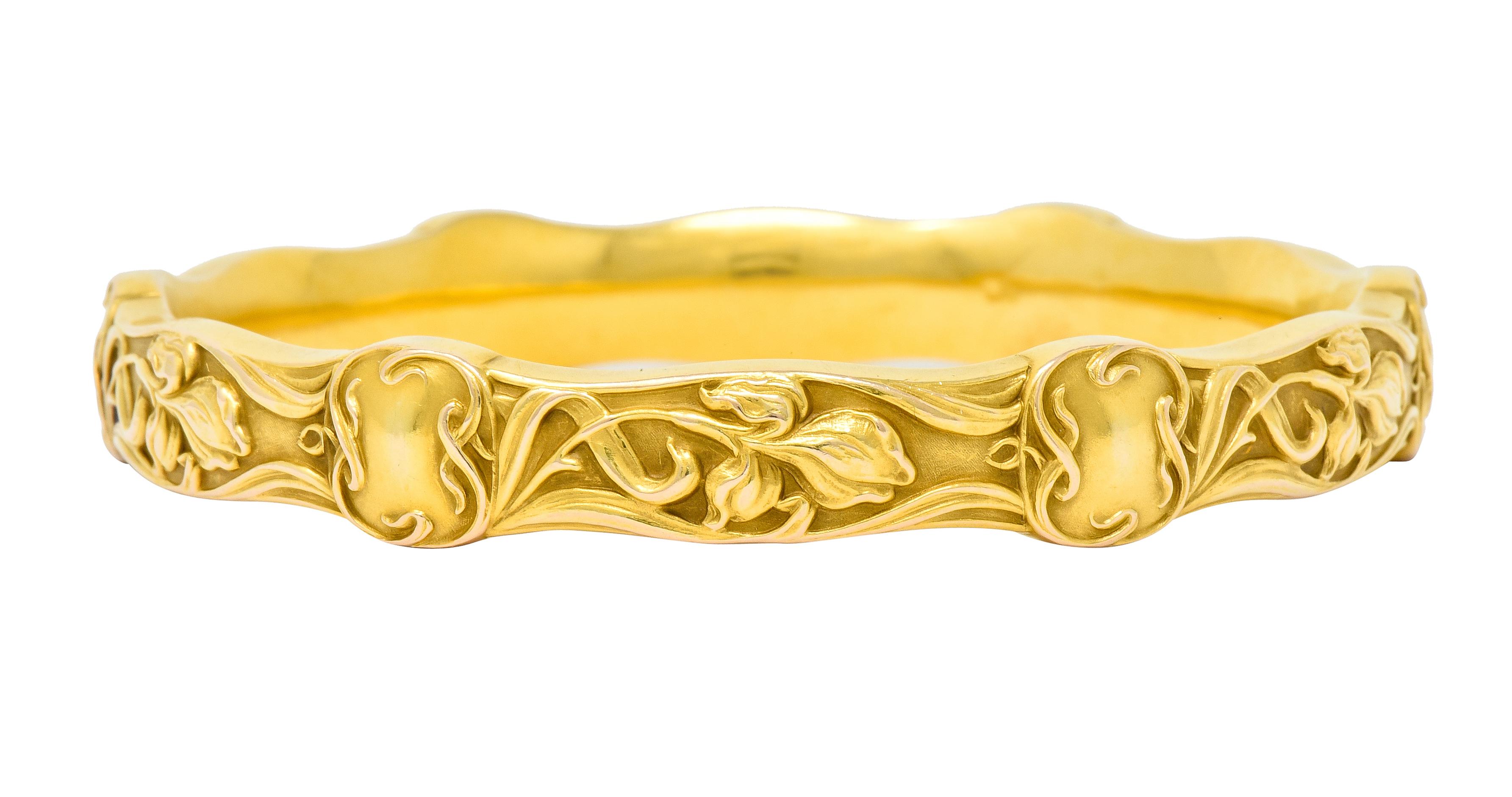 Designed as a wavy edged bangle bracelet decorated with highly rendered iris flowers and whiplash vines

Accented throughout by six cushion shaped stations with scrolled vine surrounds

One profile edge with moderate discoloration - consistent with