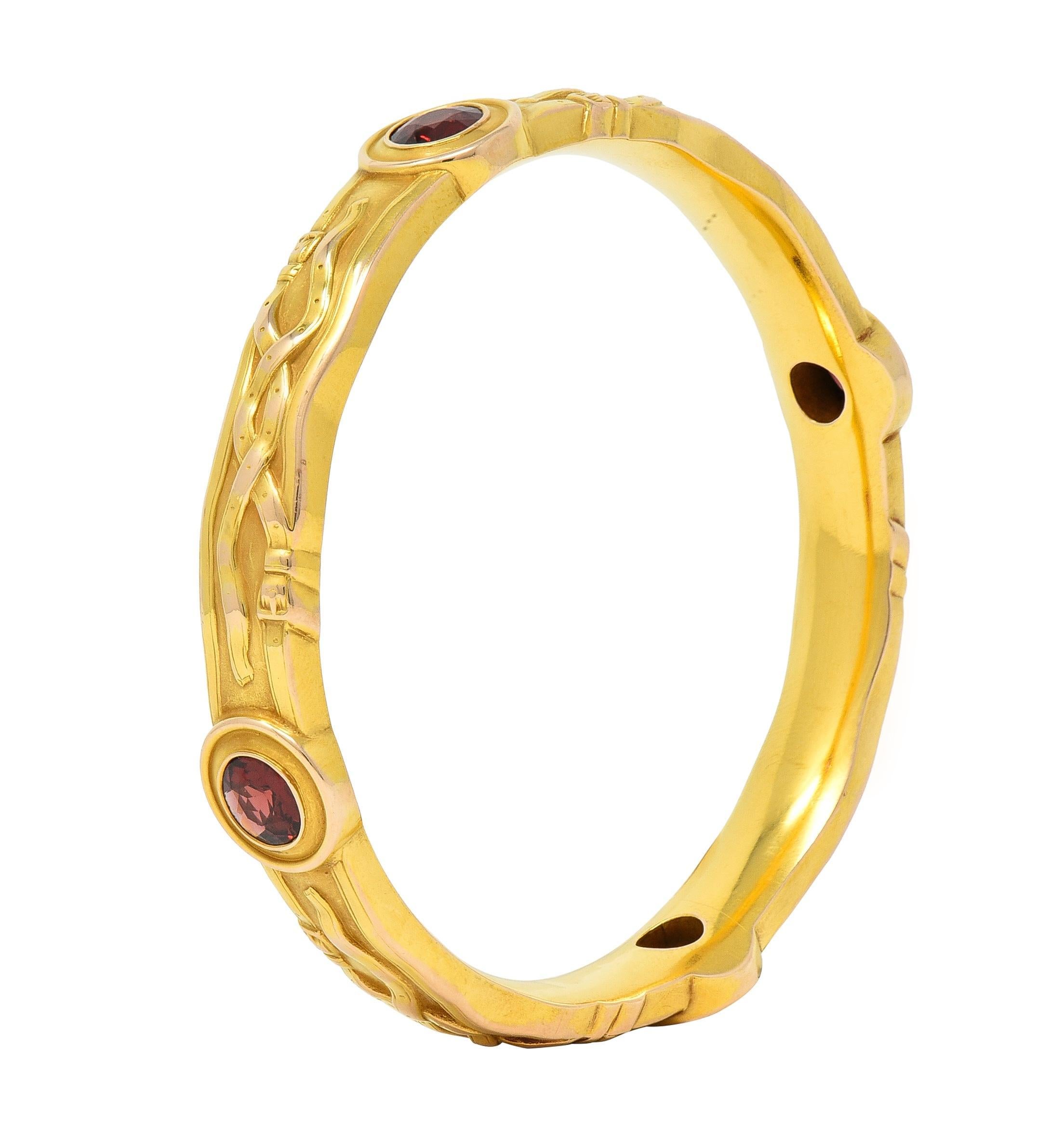 Designed as a wavy edged bangle bracelet featuring four oval stations, each bezel set by a round cut garnet, dark saturated red in color
Decorated throughout by raised stylized belts and buckles
With maker's mark for Riker Brothers and stamped 14k