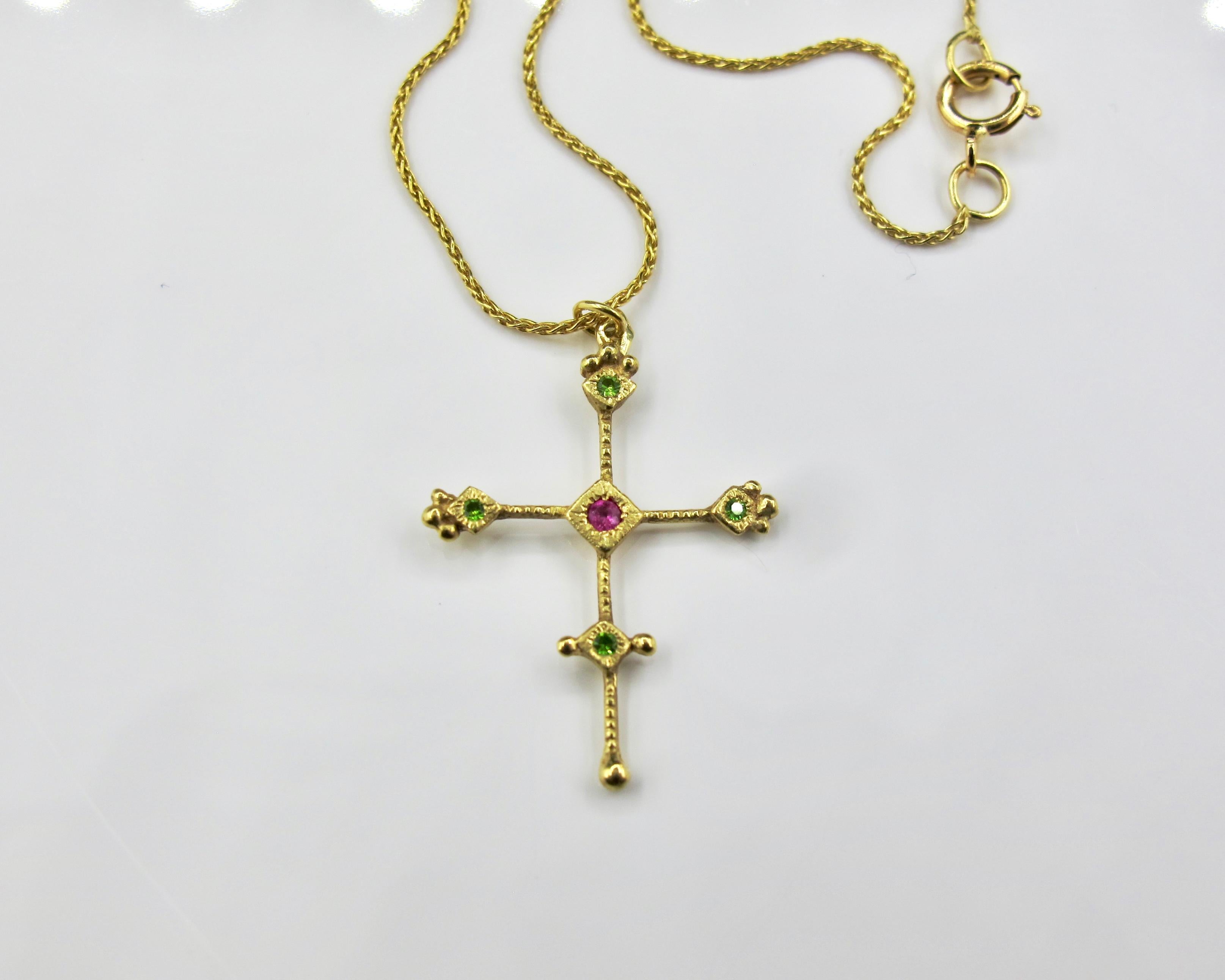 Rima Jewels signature 18k gold cross featuring a fuchsia sapphire center stone and demantoid garnets on the terminals. Strung on a 20