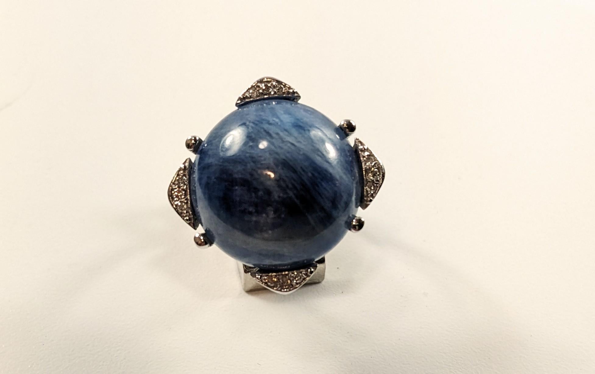 Ring 18k White Gold with Central Kyanite
White gold ring with large round kyanite star cabochon in claws bordered by four white pavede details with brilliant cut diamonds
A kyanite  17ct
12 btes  0,12 ct aprox
Ring number 17
Weight 7 gr.

IRAMA