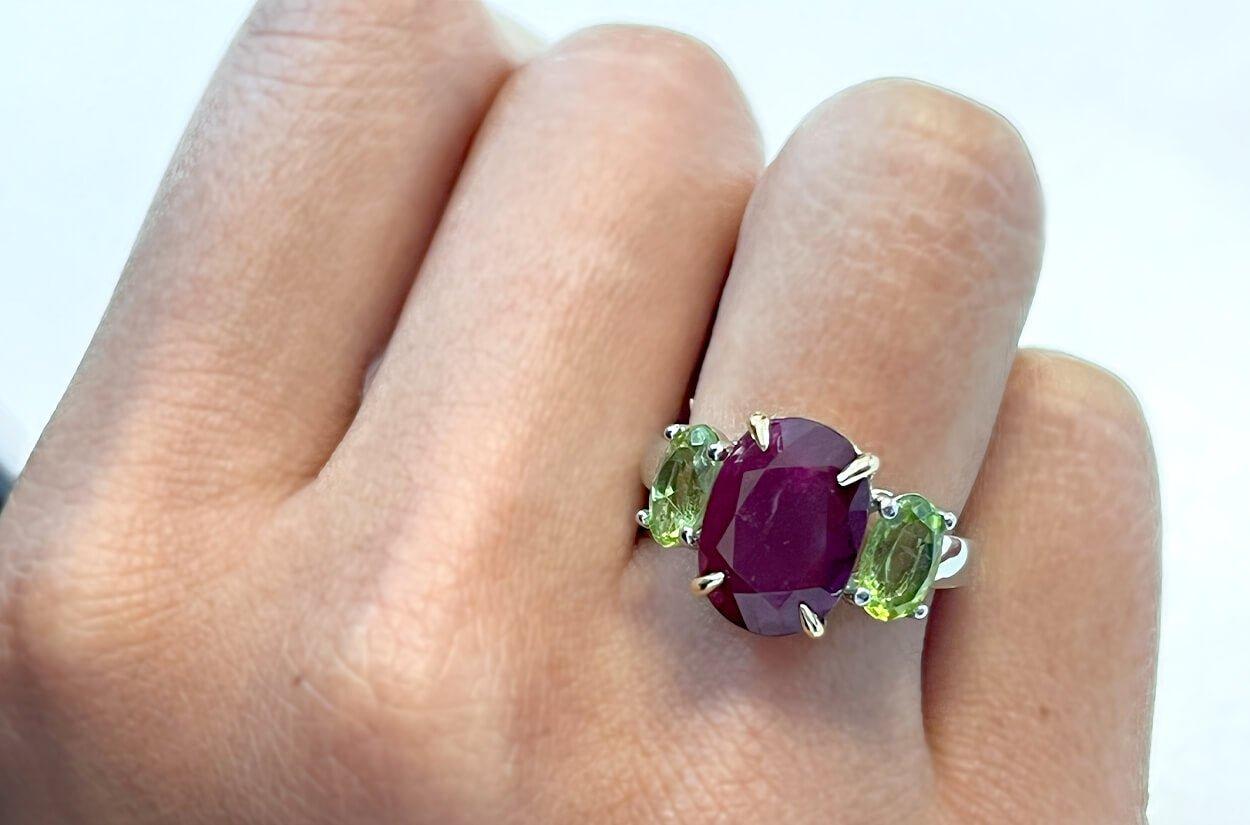 indulge in allure of this 18kt two-tone ring, featuring a resplendent GIA oval ruby at its center, exuding a deep and passionate radiance. Accompanied by two side oval peridot gemstones, this piece captures a striking contrast, forming harmonious